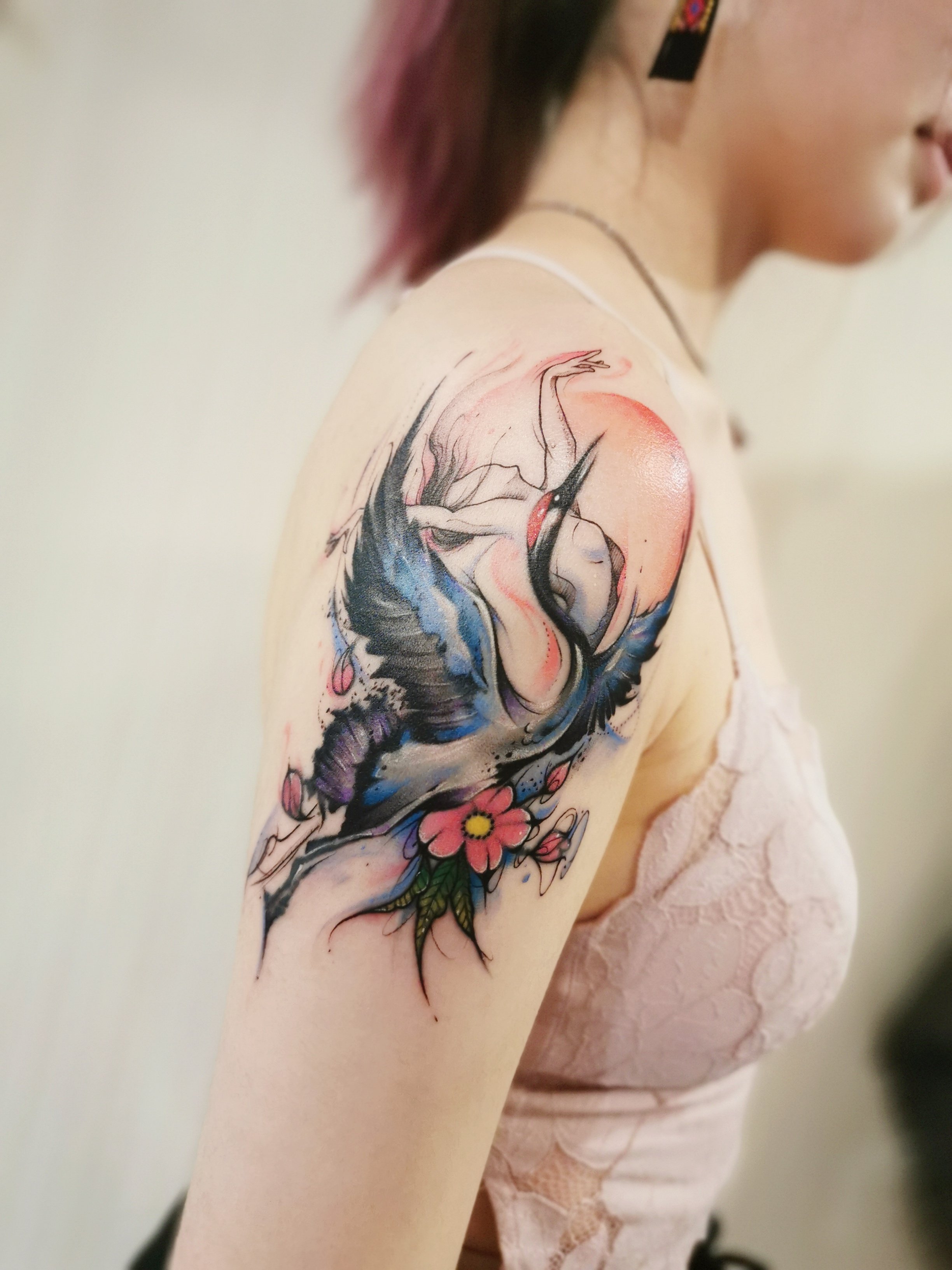 Person with a colorful tattoo of a crane and flowers on their upper arm.