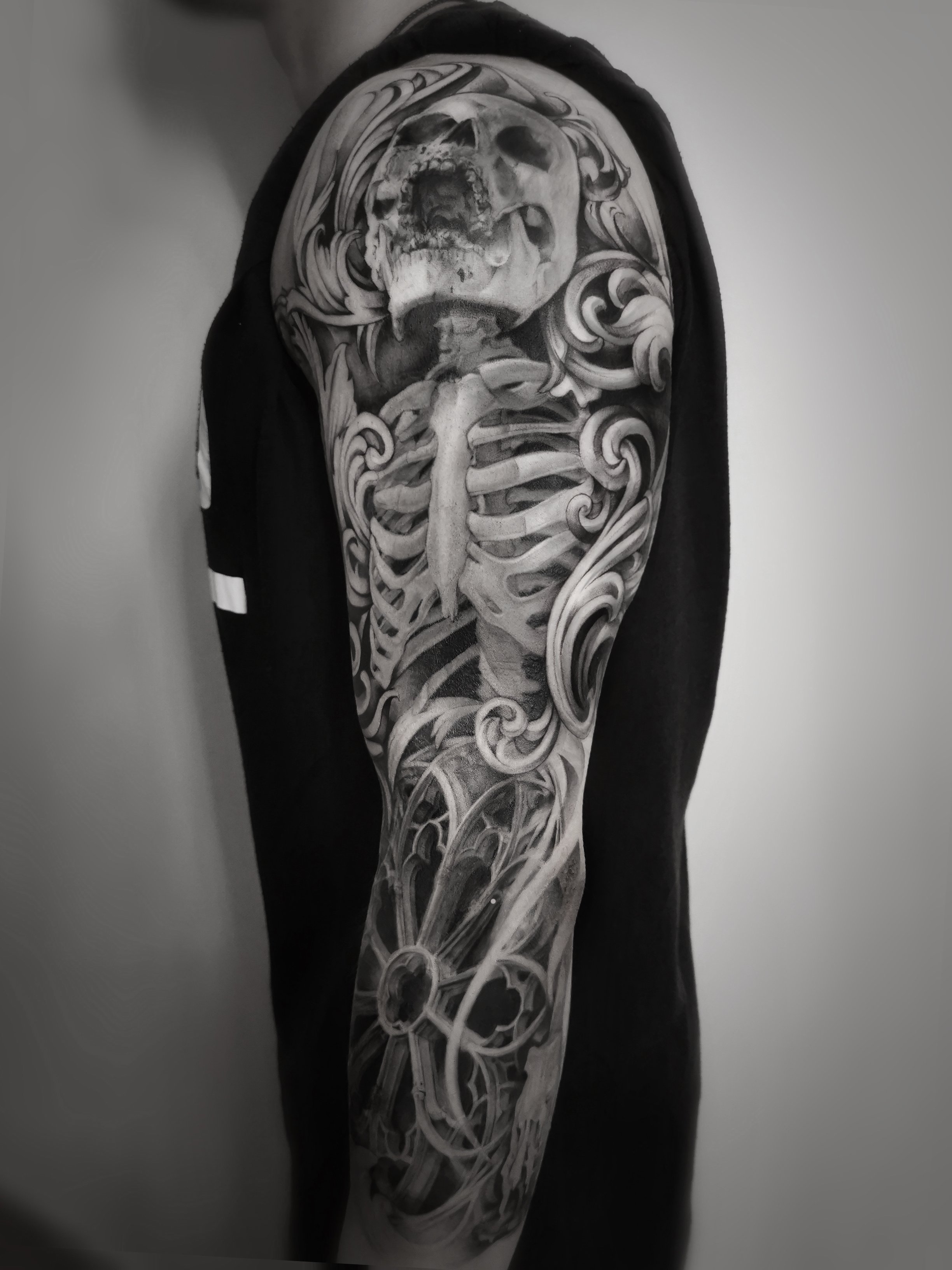 Detailed black and gray tattoo sleeve featuring a human skeleton and intricate swirls on an arm.