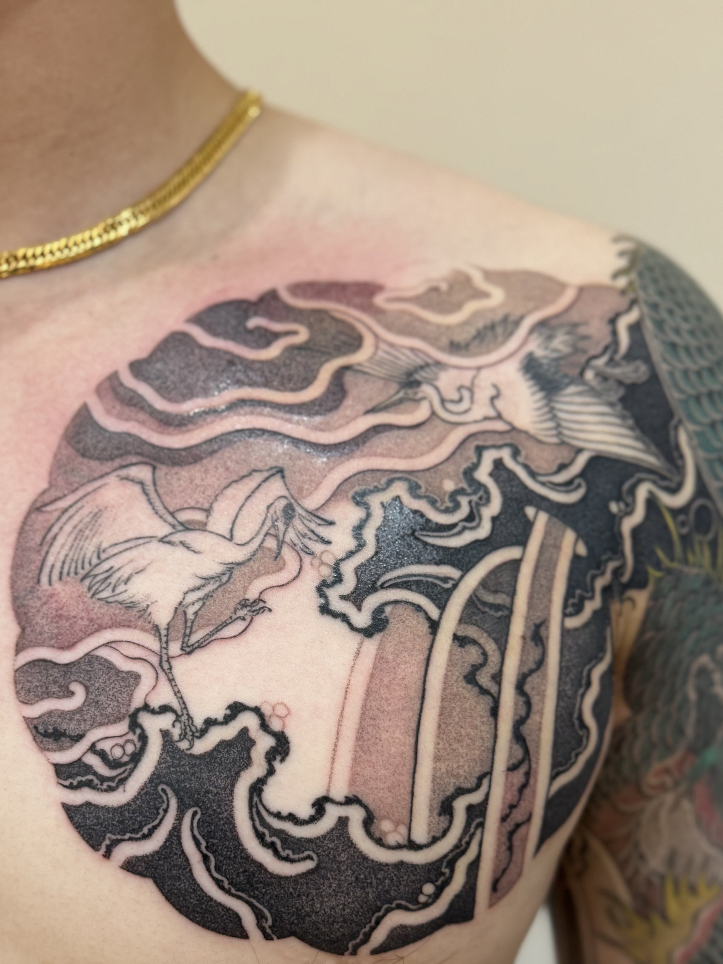 Tattoo of two birds flying among clouds and stylized elements on a person's shoulder.