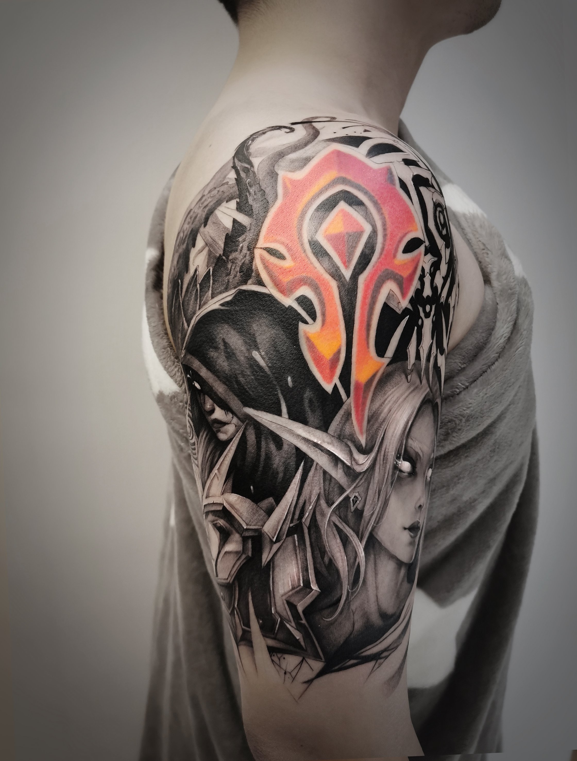 Arm tattoo featuring a stylized Horde emblem in vibrant reds and oranges, blending into a detailed, monochrome illustration of fantasy characters and elements, likely inspired by a popular role-playing game.