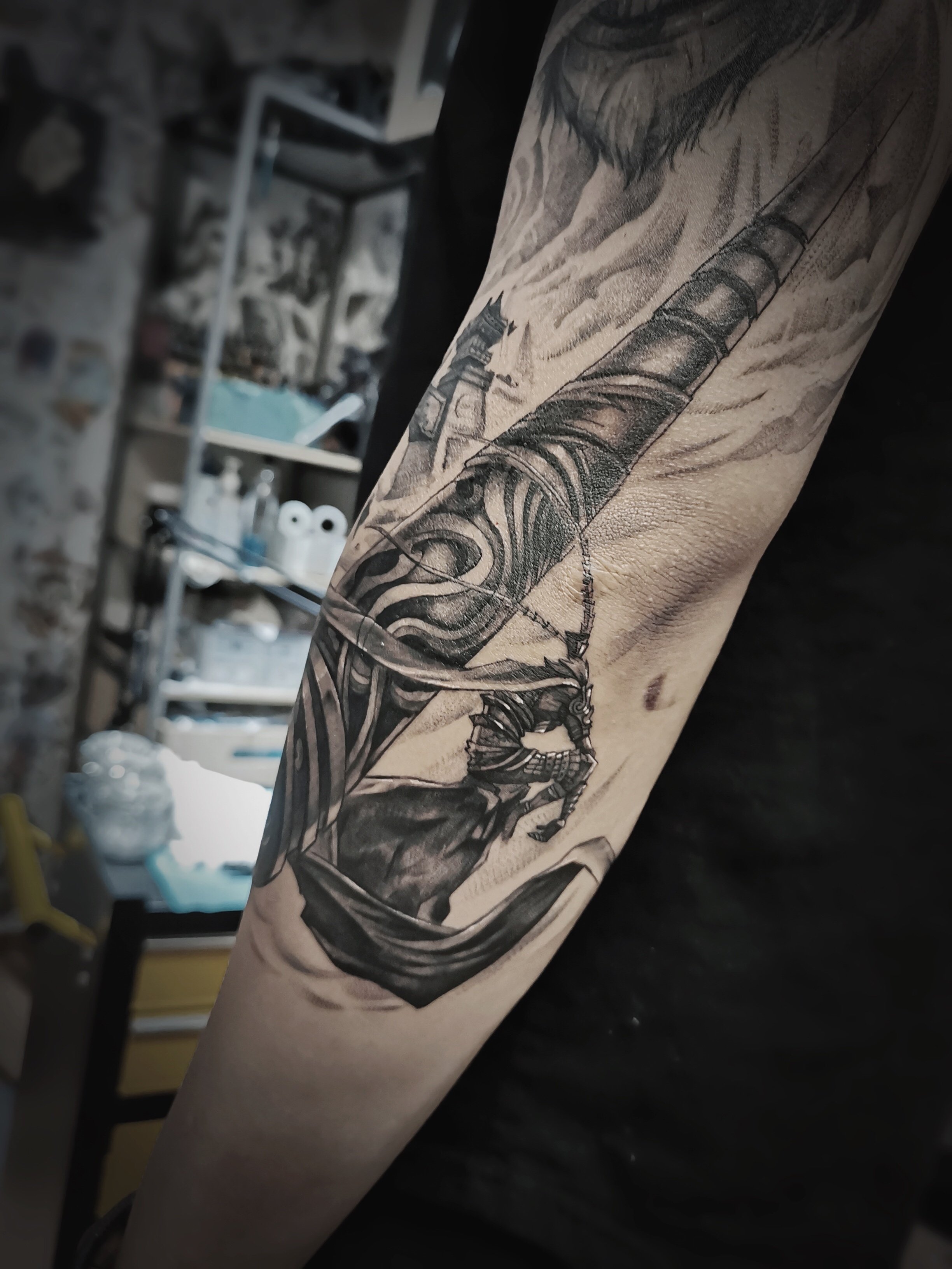 Detailed arm tattoo featuring a warrior with a sword and armor, with intricate designs, against a blurred background.