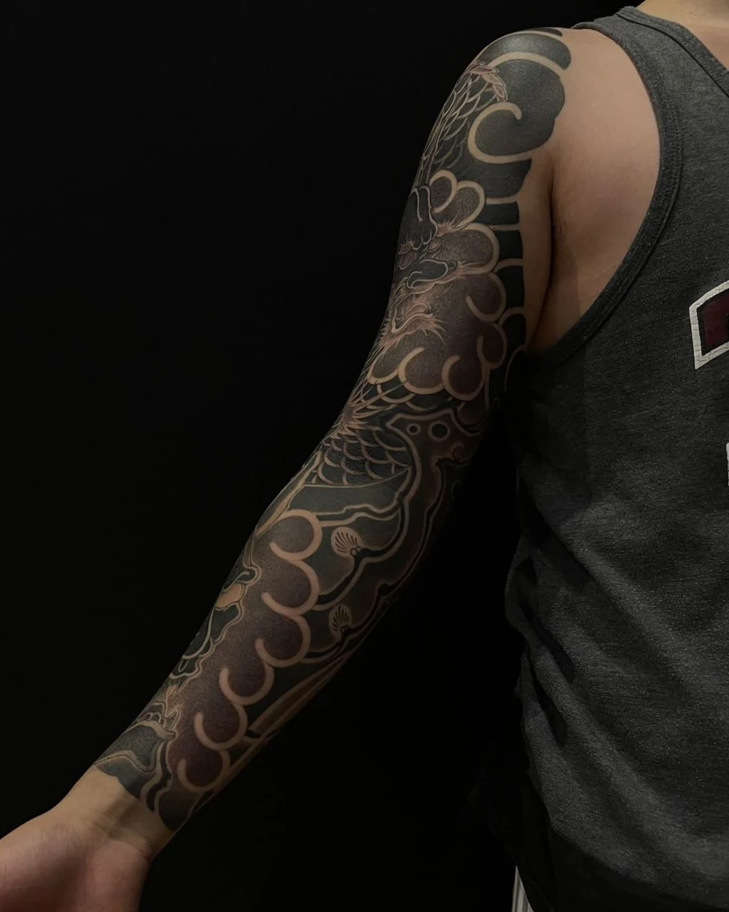 Arm with sleeve tattoo featuring intricate dark and light patterns, wearing a sleeveless shirt.