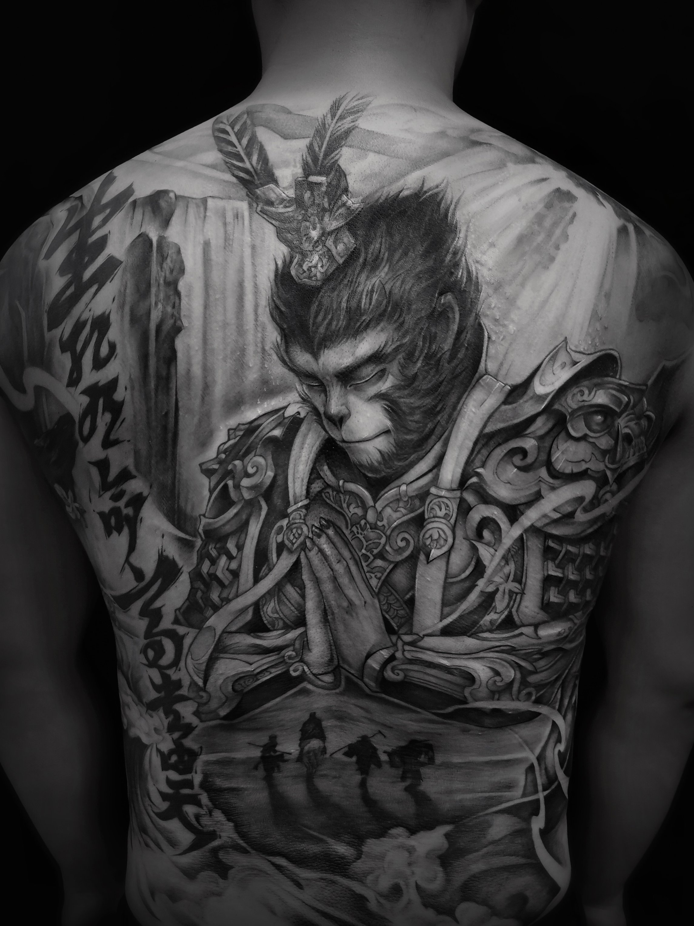 Intricate black and white tattoo on a person's back featuring a warrior monkey in armor, surrounded by artistic patterns and symbols, with a scene of travelers below.