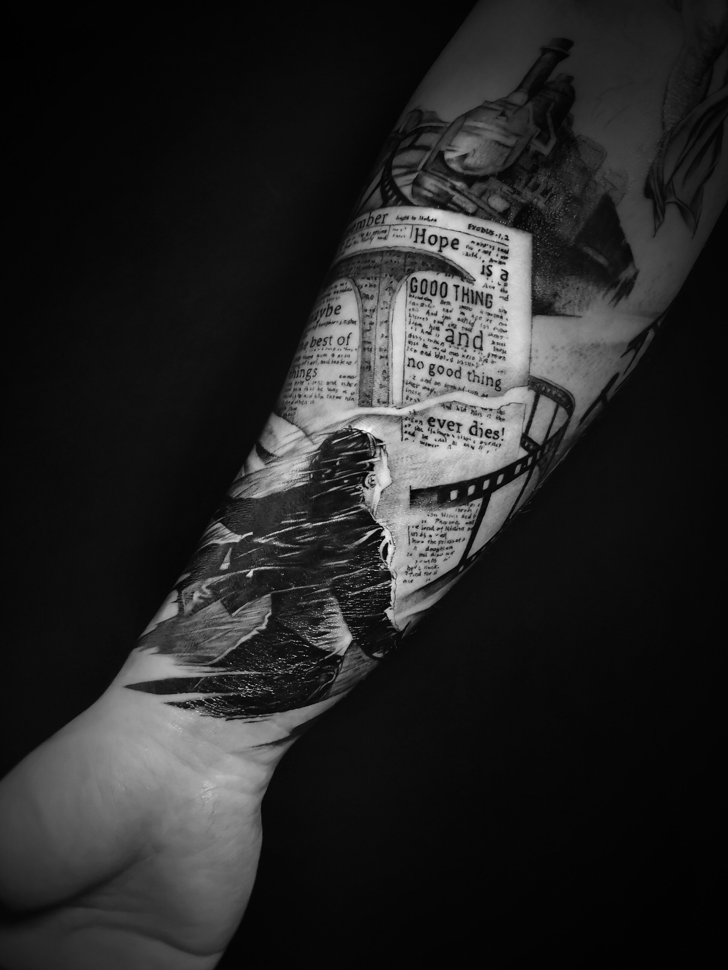 Forearm tattoo with black and white design including a quote, image of a steam train, pages of text, and abstract elements. Tattoo extends from the wrist upwards.