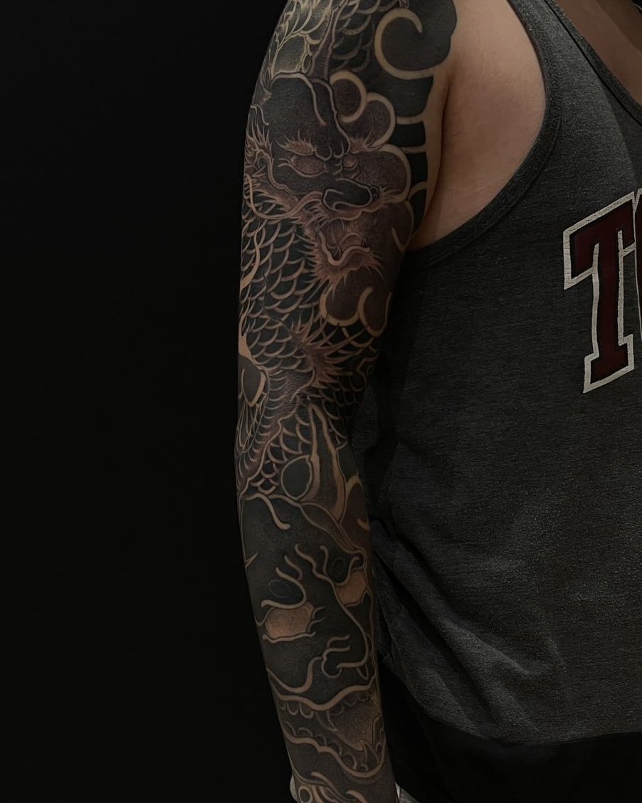 Tattoo sleeve with dragon design on person's arm wearing a gray tank top.