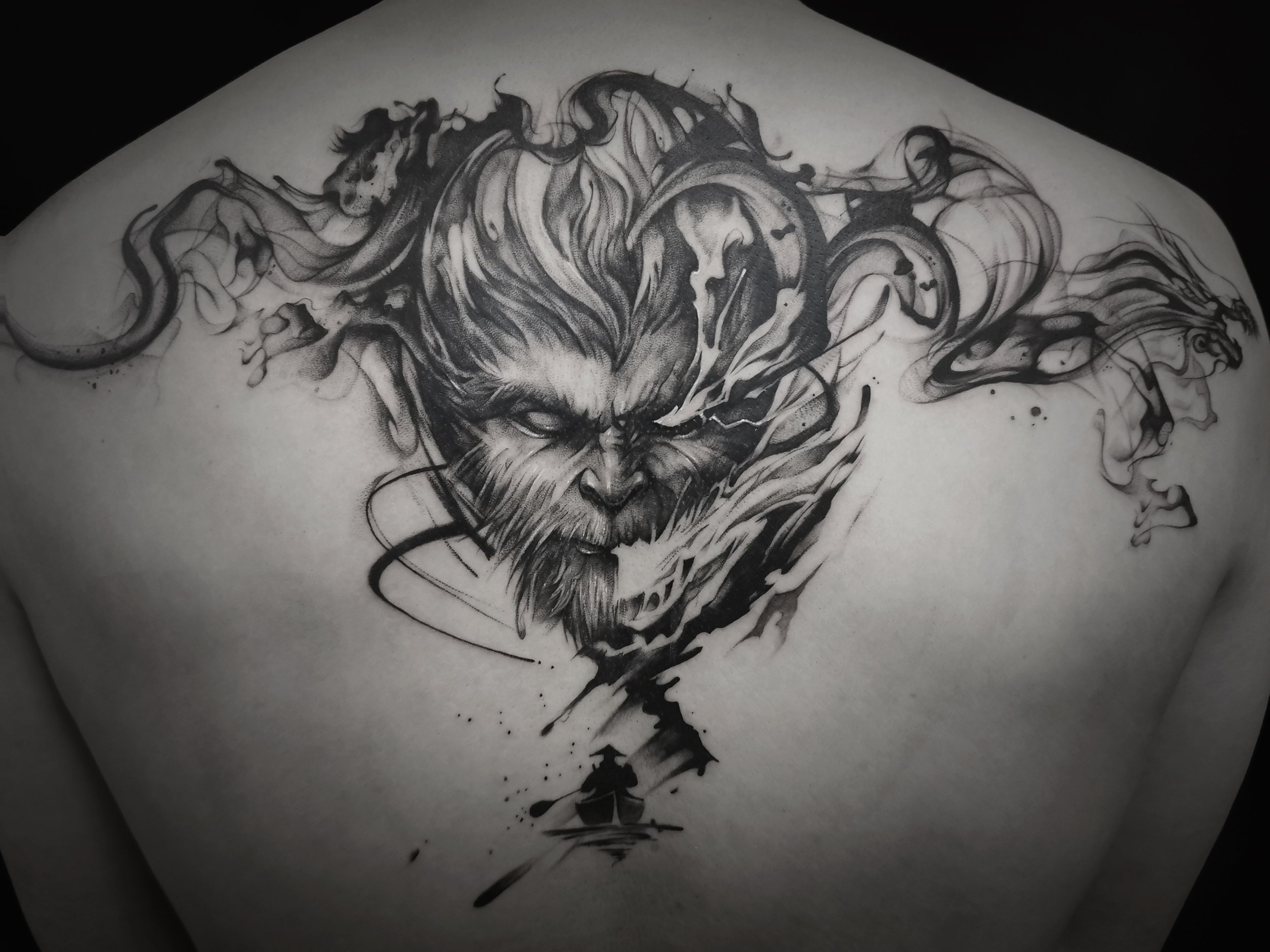 Black and gray tattoo of a werewolf face with abstract design on a person's back.
