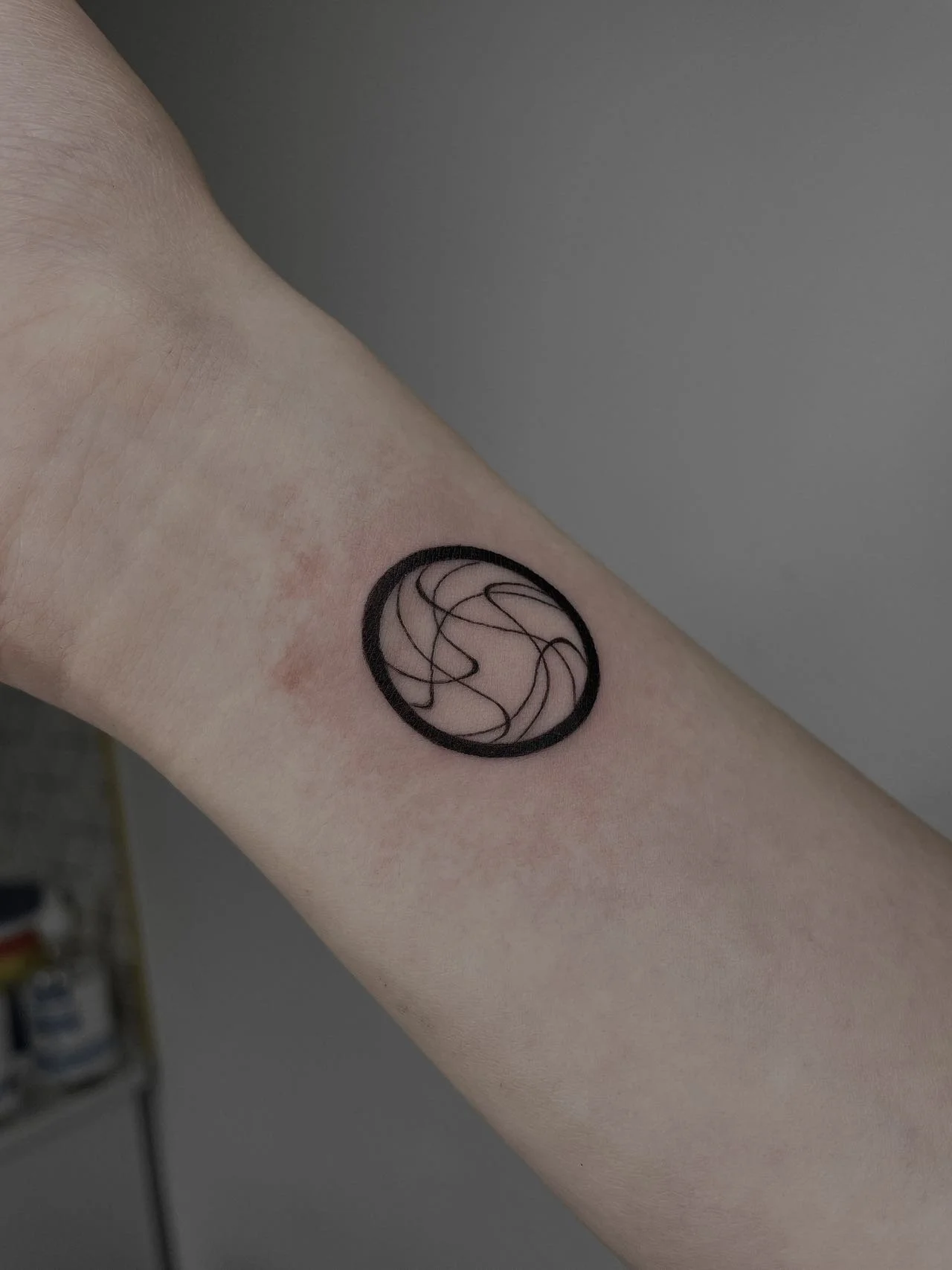 Minimalist line art tattoo on forearm with circular design.