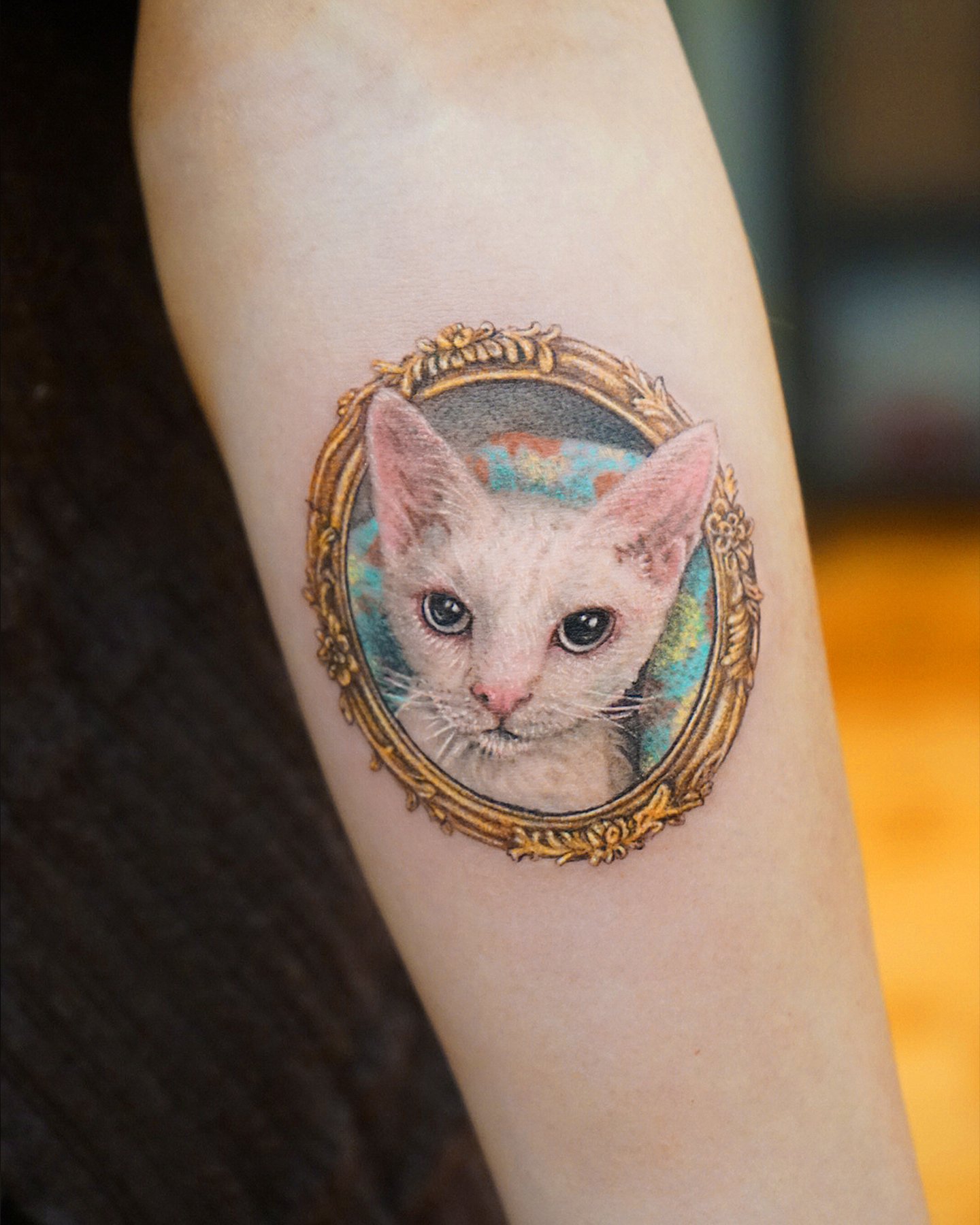 Tattoo of a hairless cat framed in an ornate oval frame on a person's skin.