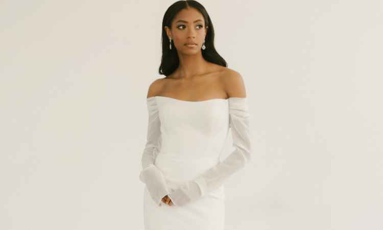 Bride wearing an elegant off-the-shoulder minimalist wedding dress with long sleeves and a clean silhouette.