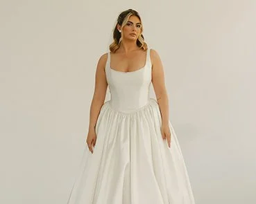 Woman wearing a white wedding dress with a fitted bodice and full skirt, standing against a plain background.