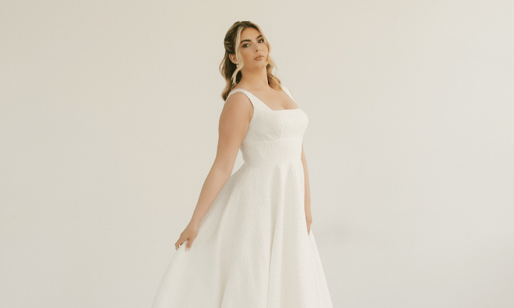 Bride wearing a simple A-line wedding dress with wide straps, a square neckline, and textured fabric.