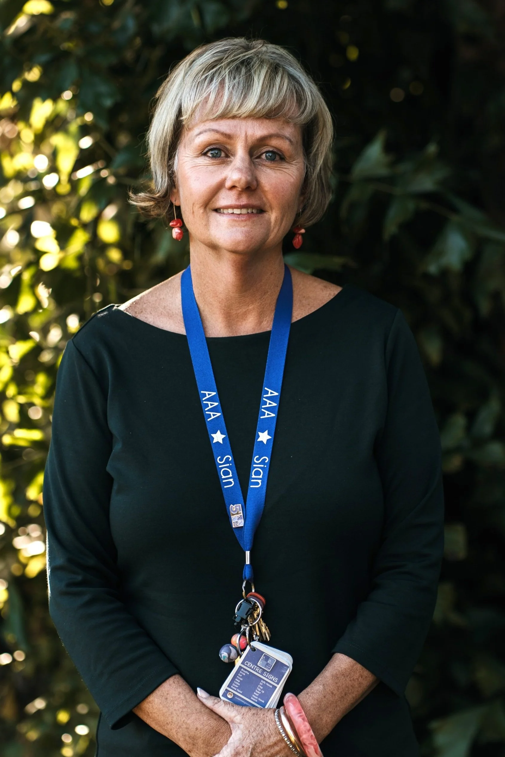 A woman with blonde hair and a floral blouse smiling outdoors, wearing a blue lanyard with 'AAAI' and 'Sign' written on it.