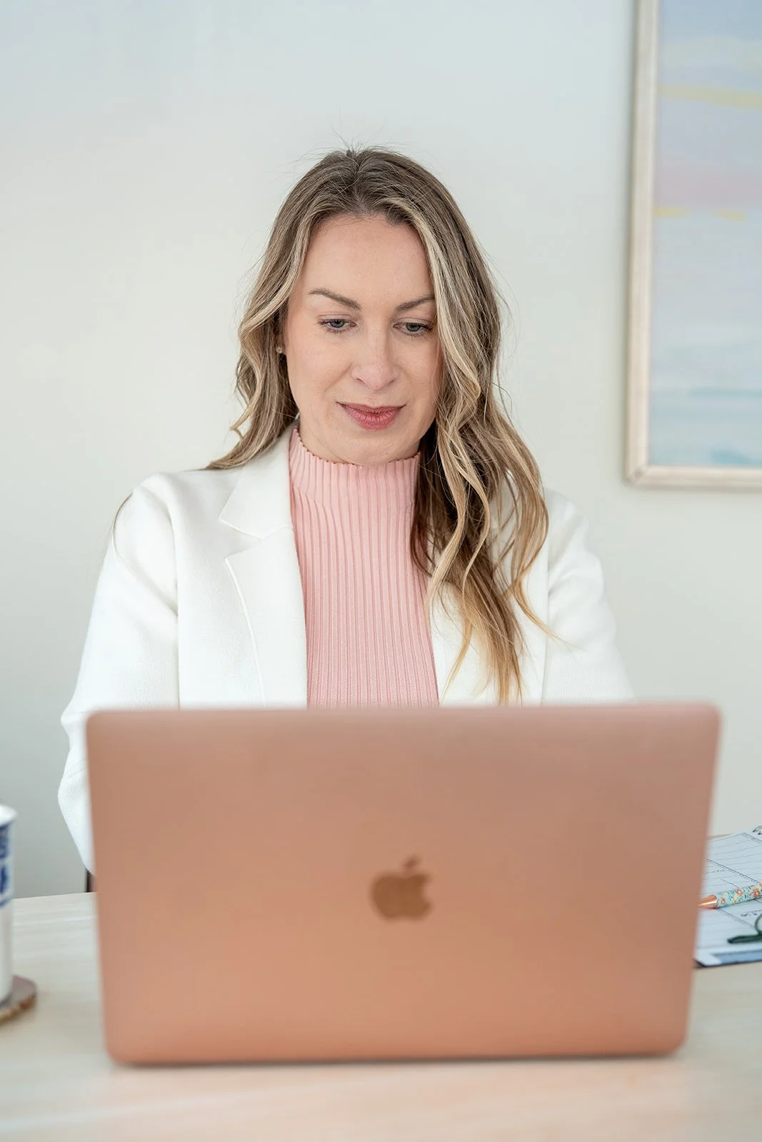 Maura sitting at her desk, working on rose gold laptop