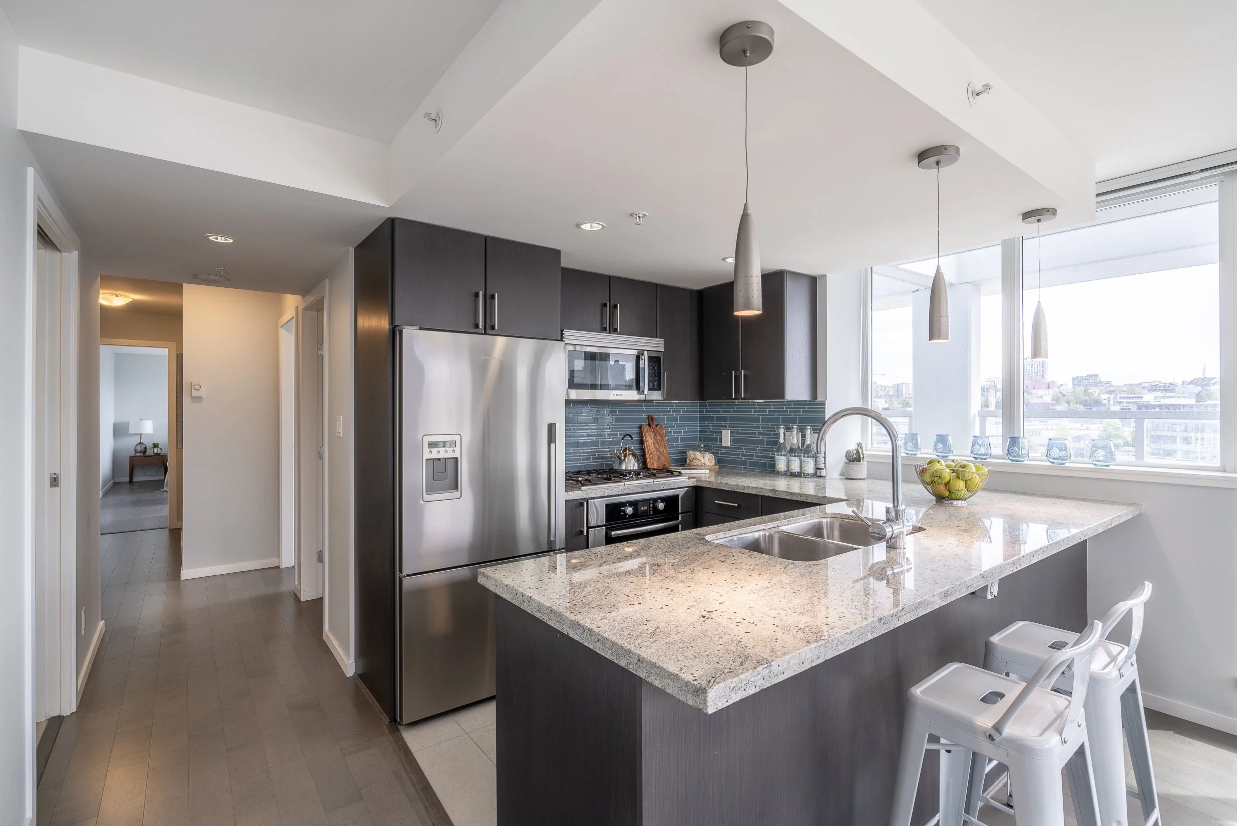 Modern kitchen with granite countertops, stainless steel appliances, dark cabinets, pendant lights, and a window view.