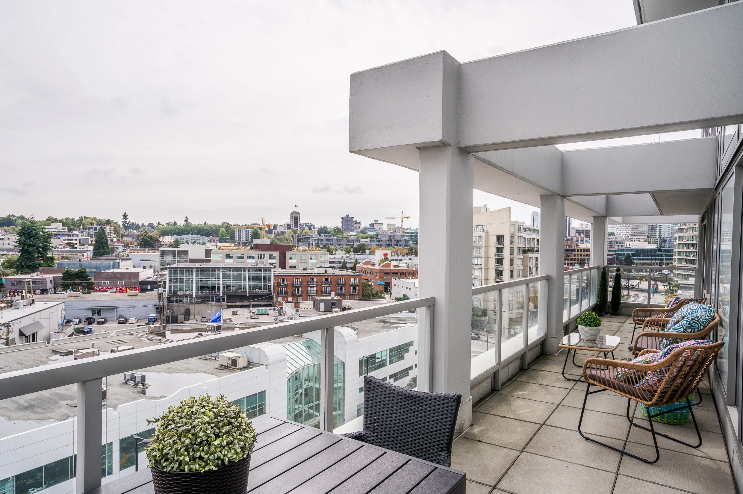 Balcony with outdoor chairs and table overlooking an urban cityscape with buildings and construction cranes.