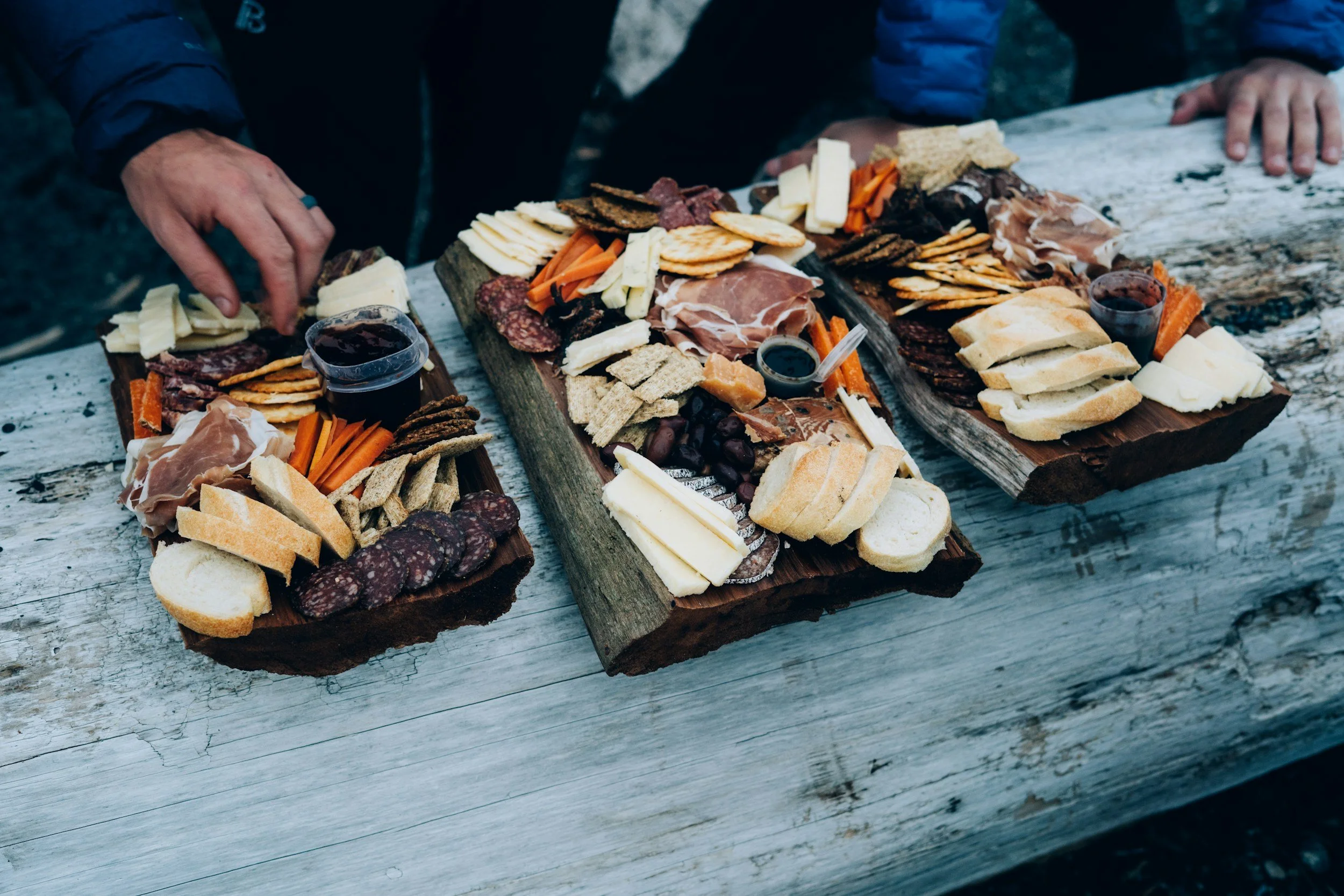 Charcuterie boards with assorted cheeses, cured meats, crackers, vegetables, and small cups of red wine on rustic wooden tables.