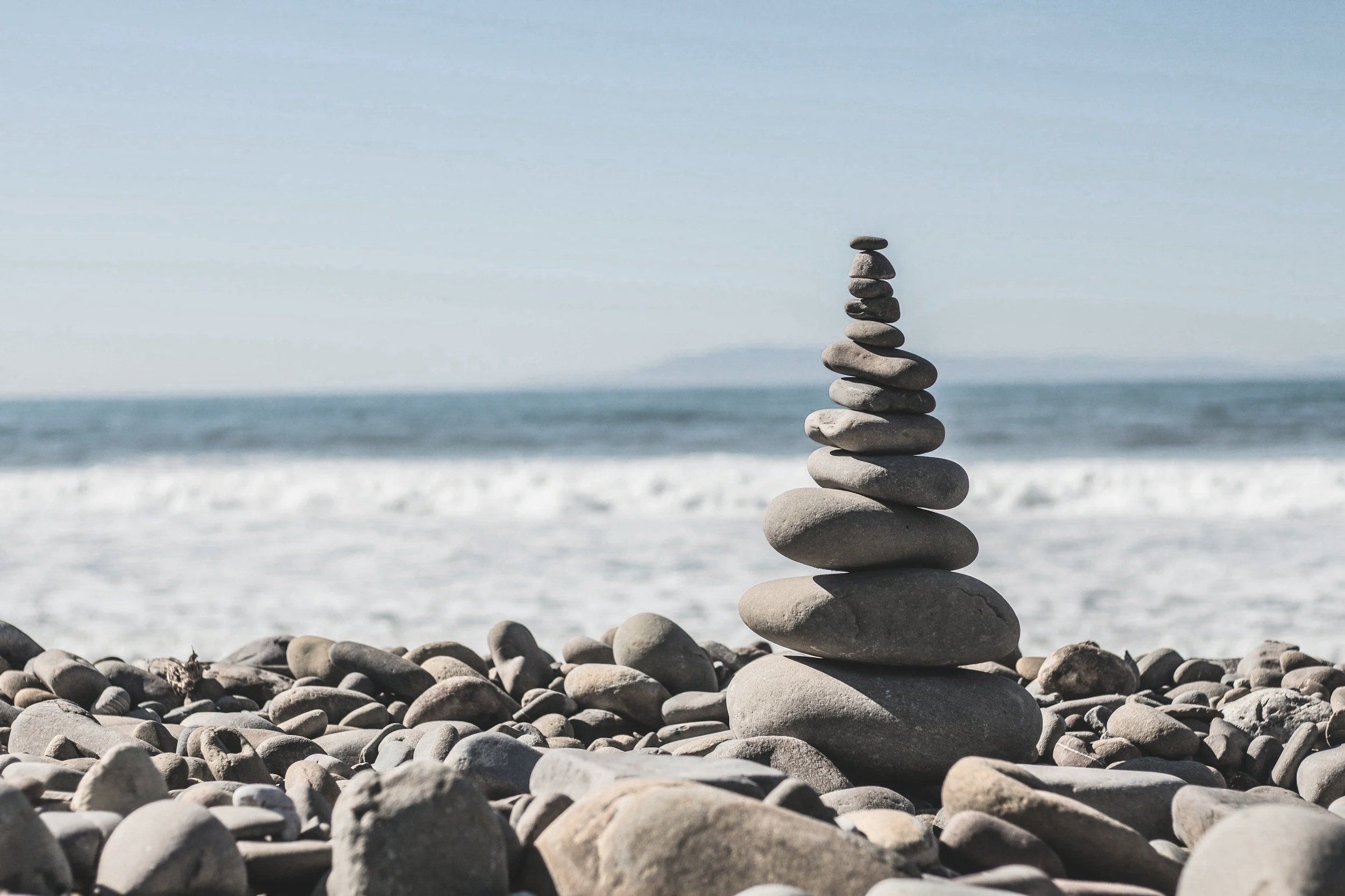 Stack of smooth gray stones balanced on a beach with the ocean and sky in the background.