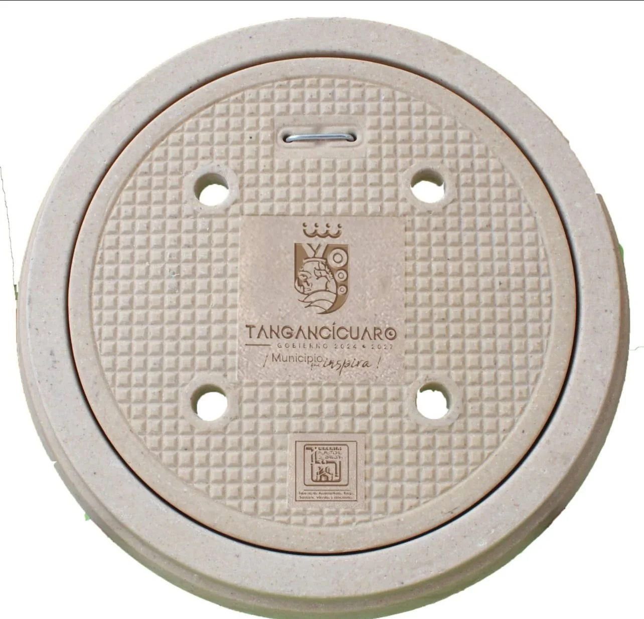 Tapa de alcantarilla de color beige con el escudo y el logotipo del municipio de Tangancícuaro, Michoacán, México.