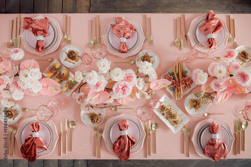 A pink-themed table setting with plates, gold utensils, pink and white napkins, floral centerpieces, and small desserts and snacks.