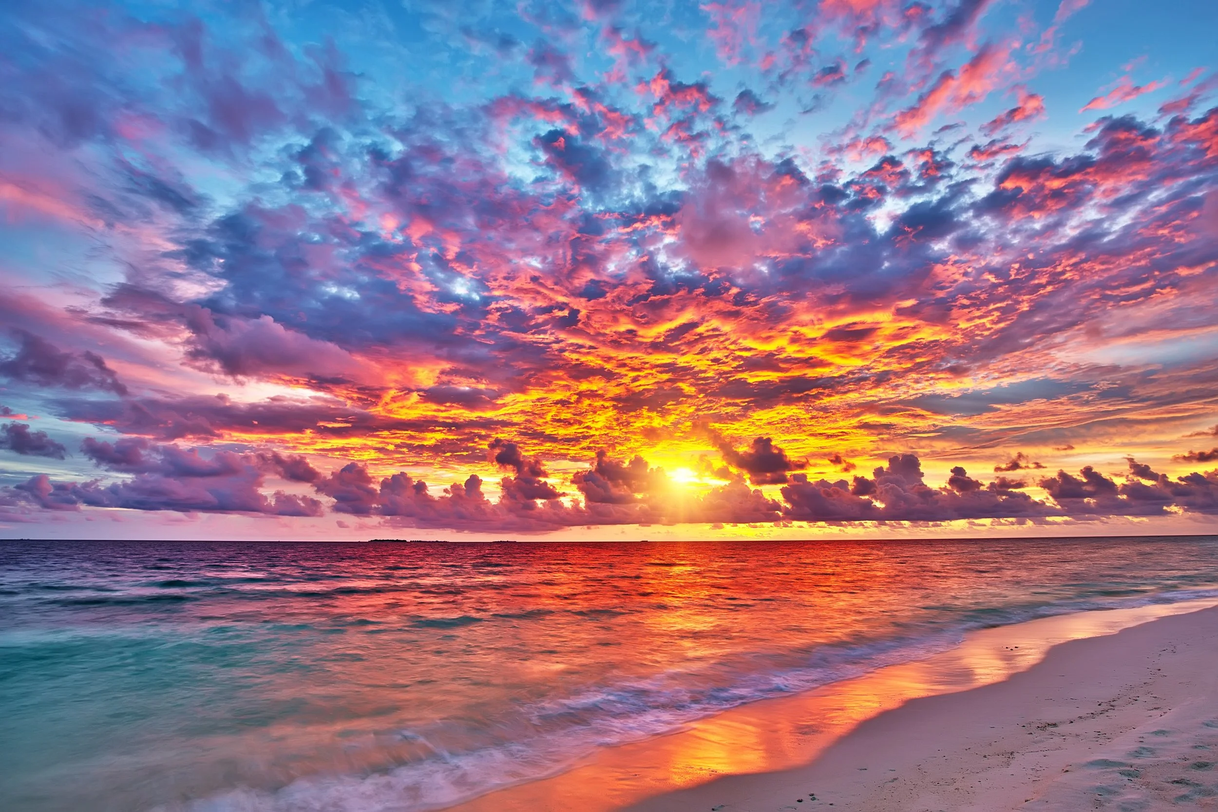 Sunset over the ocean with colorful clouds and a sandy beach in the foreground.