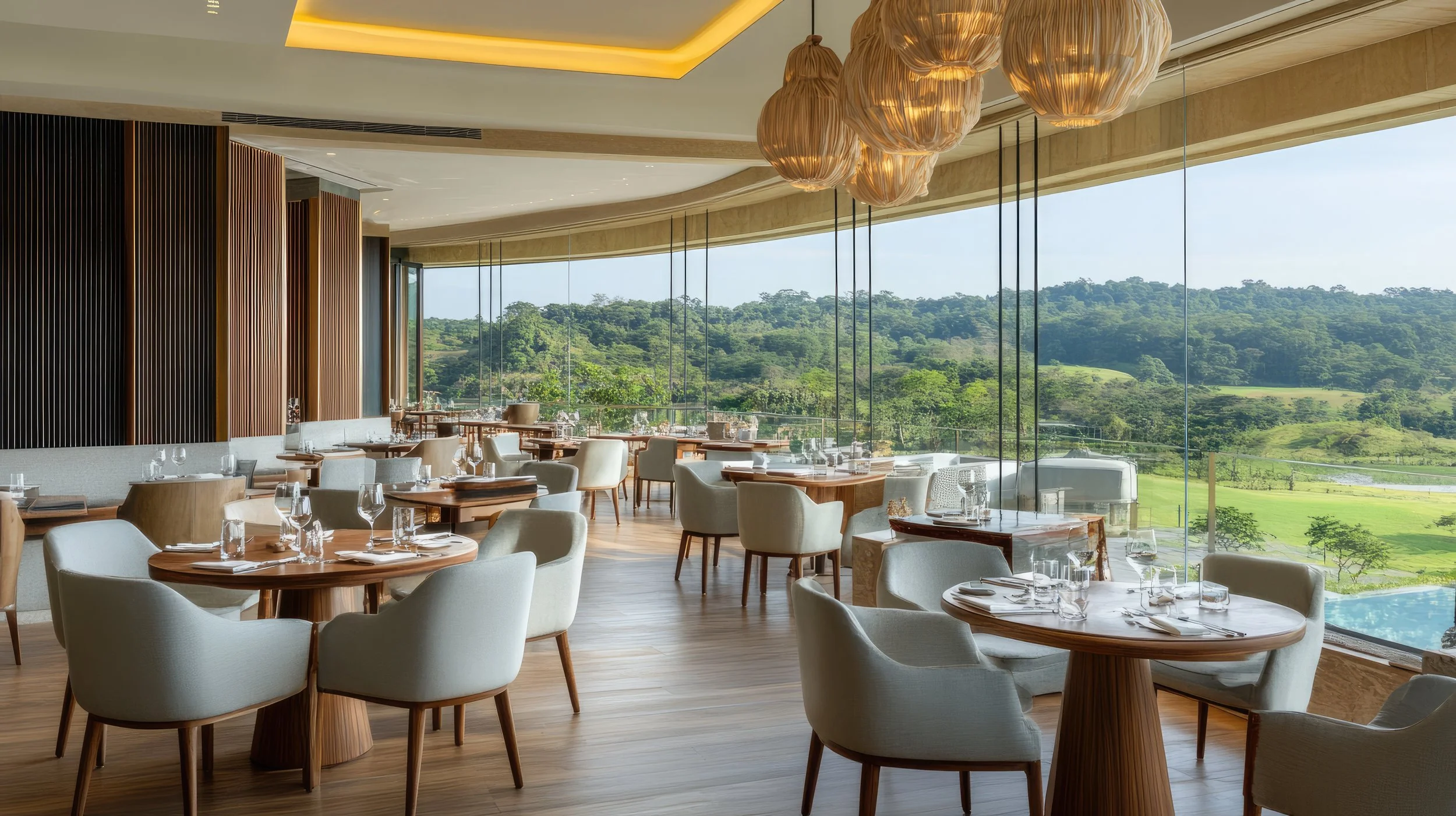 Elegant restaurant interior with round wooden tables set with glassware and white napkins, cream-colored chairs, large floor-to-ceiling windows showcasing a lush green landscape, wooden wall accents, and hanging light fixtures.