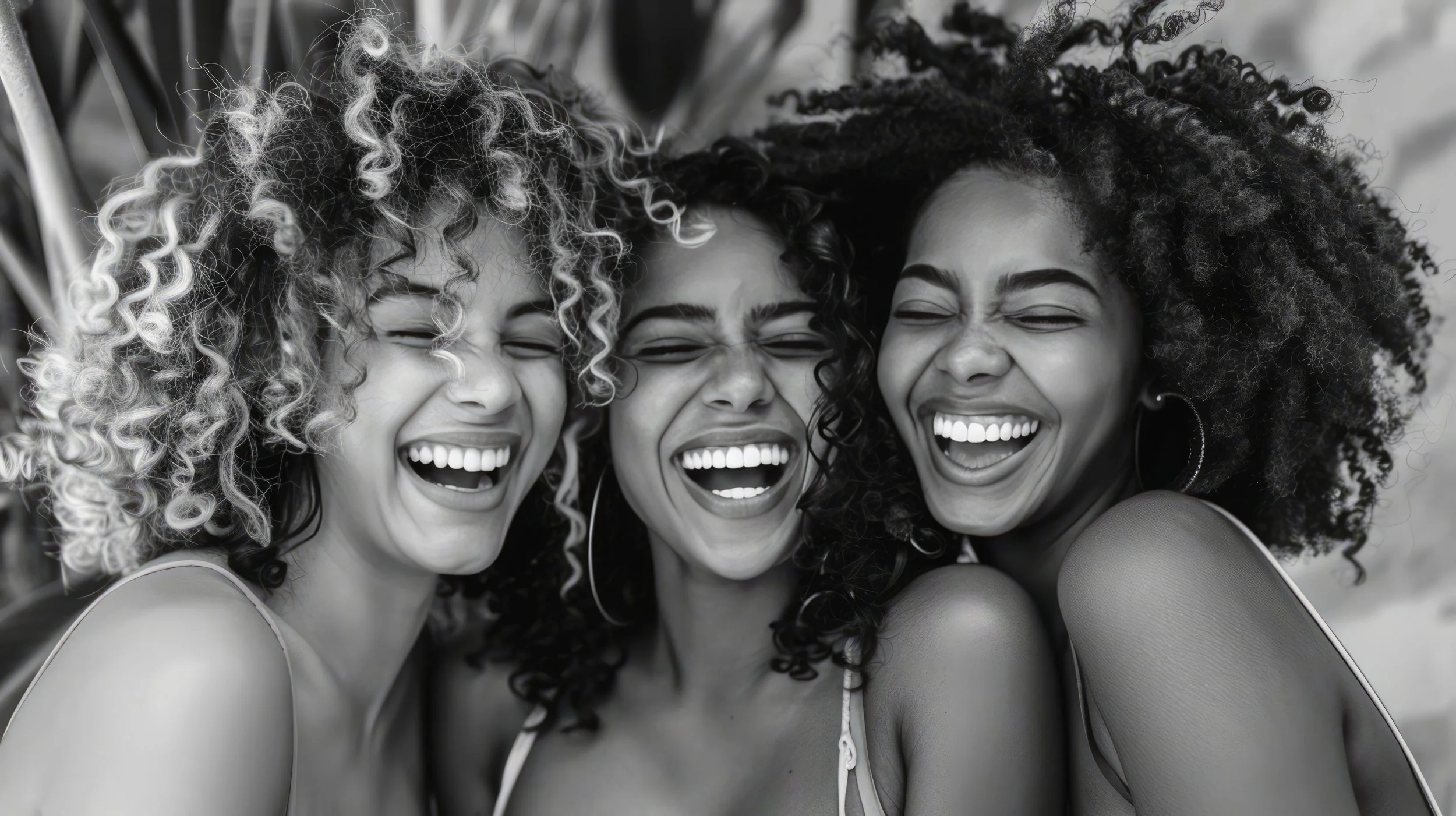 Close-up of three women with curly hair laughing together in a black-and-white photograph.