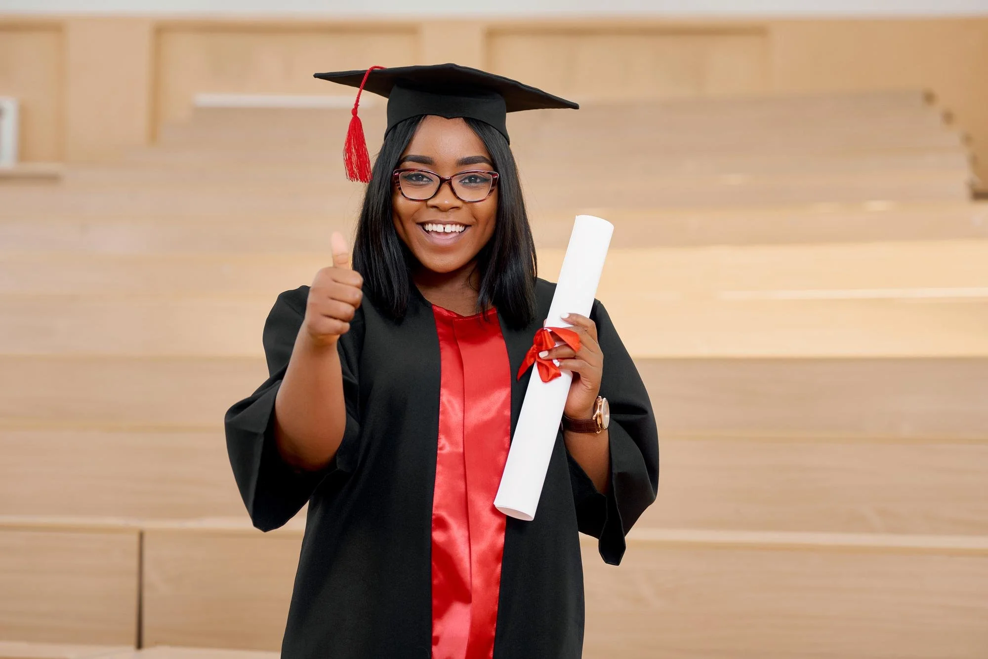 Graduate wearing cap and gown holding diploma, giving thumbs up.