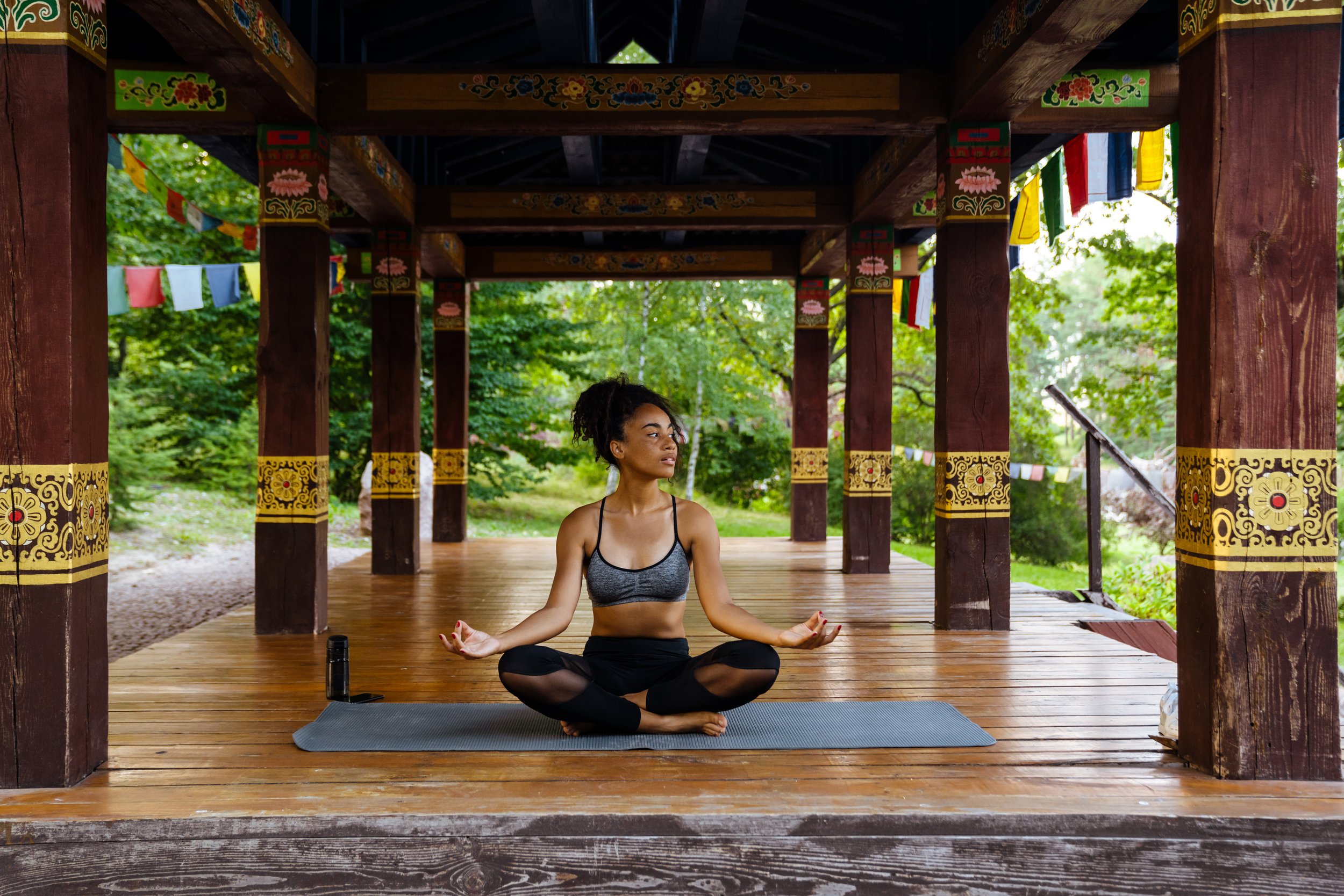 Woman meditating in a wooden pavilion with colorful Tibetan prayer flags.