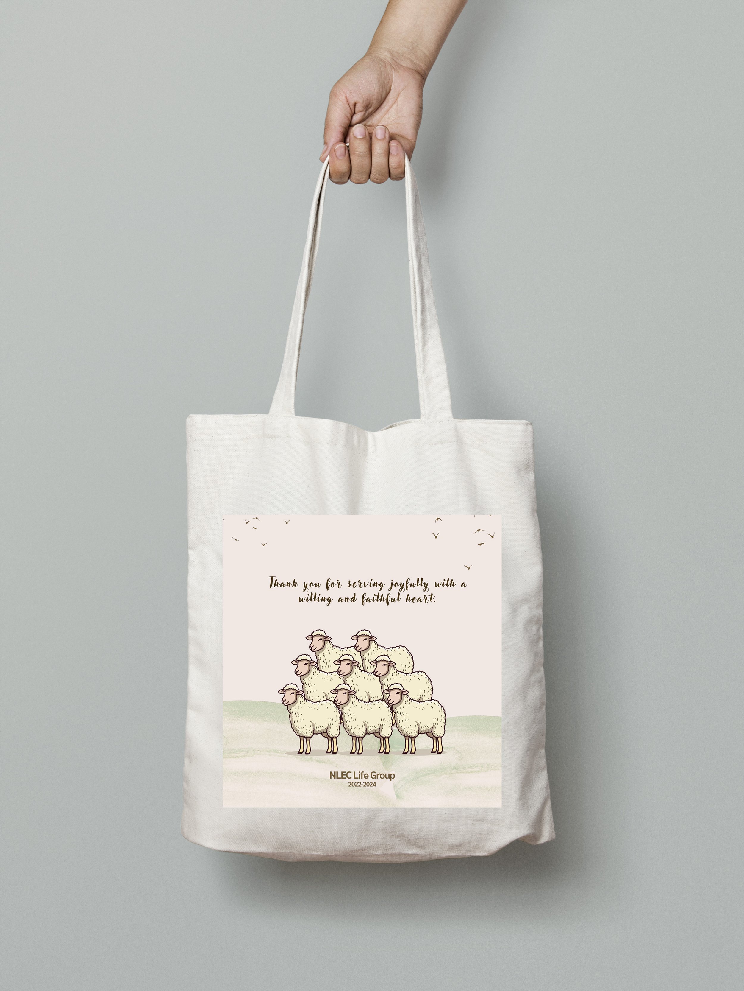 Hand holding a tote bag with an illustration of six sheep and text reading "Thank you for serving joyfully, with a willing and faithful heart. NLEC Life Group 2022-2024."