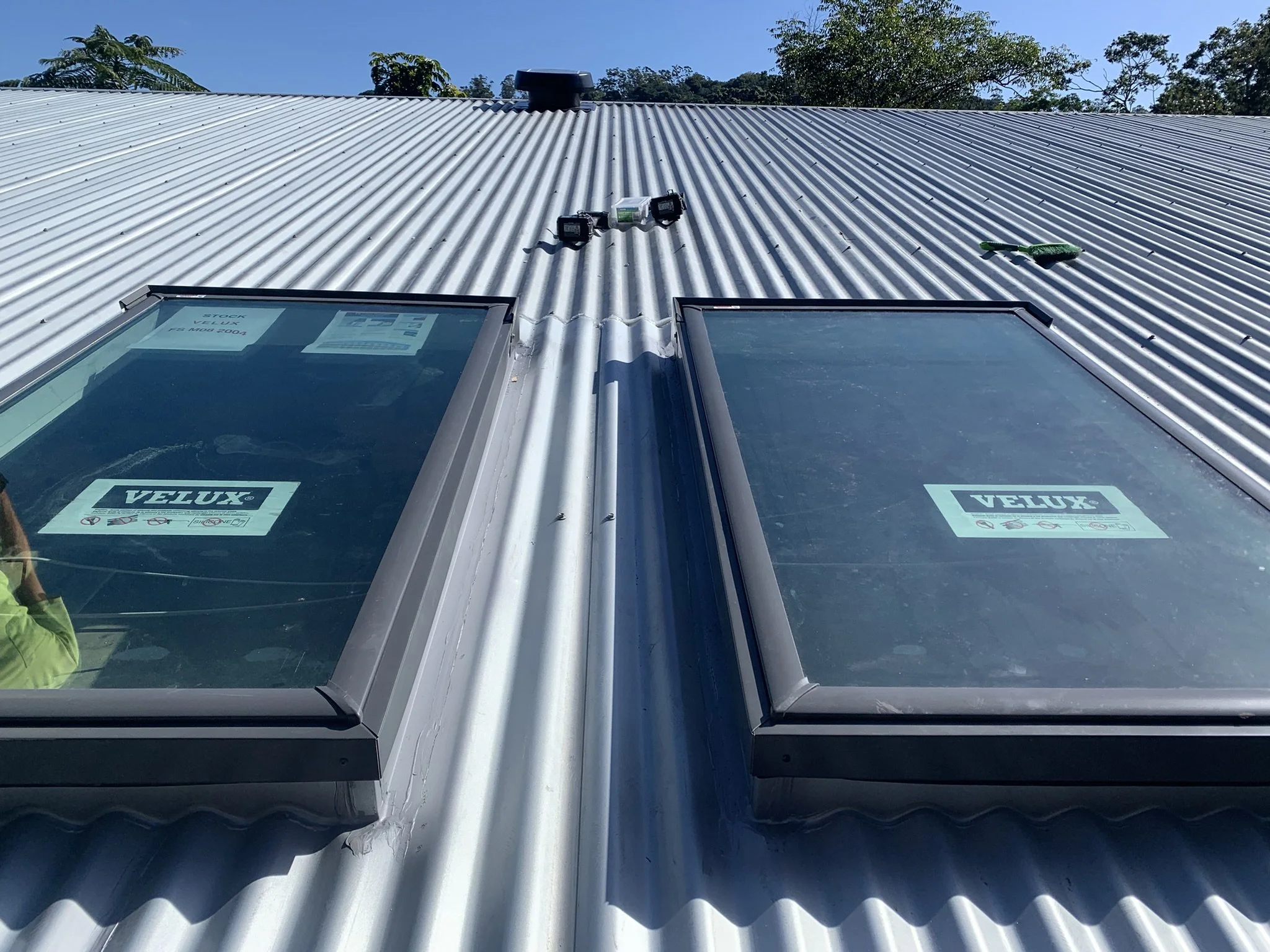 Two Velux skylights installed on a corrugated metal roof under a clear blue sky.