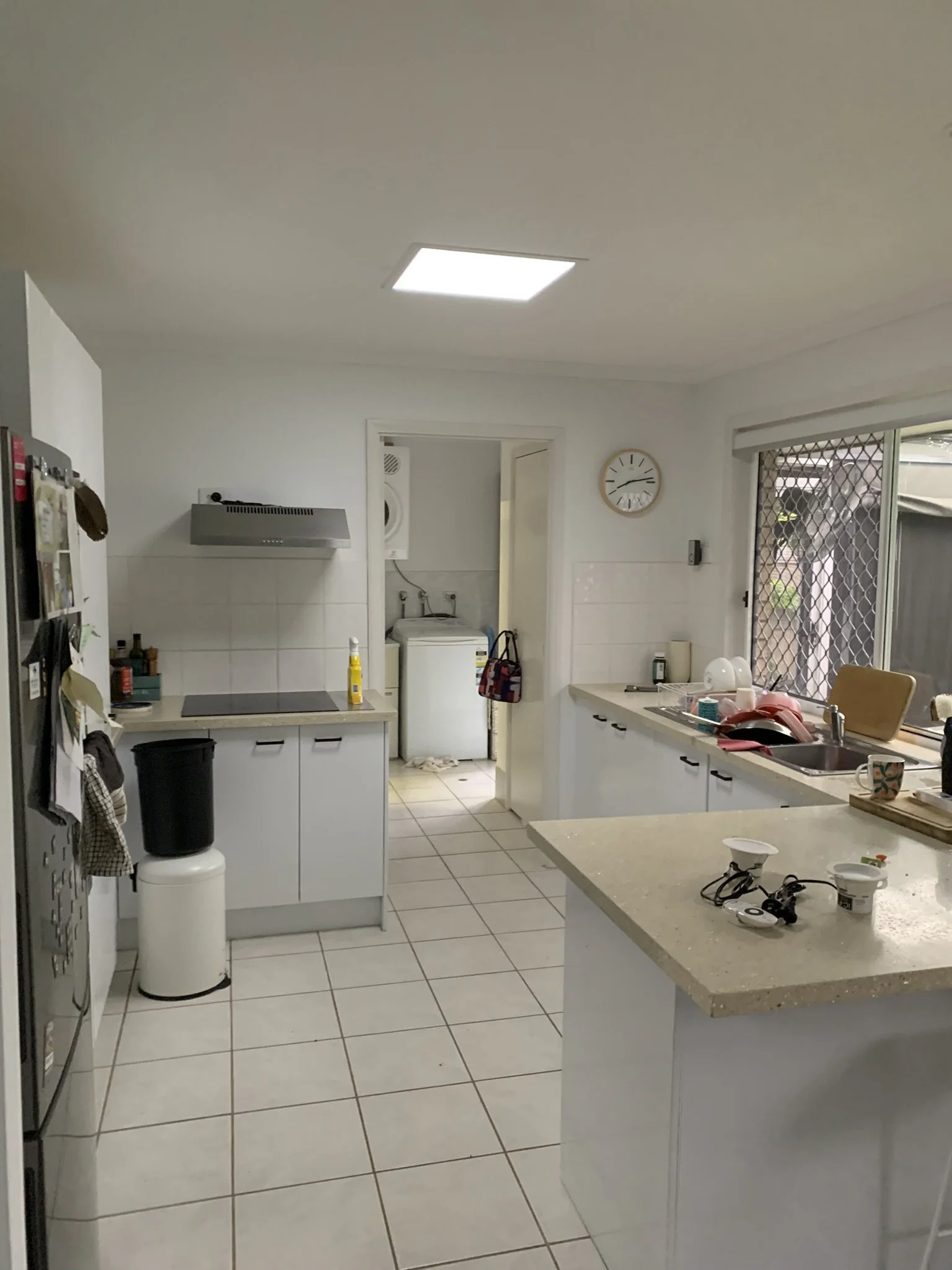 Modern kitchen with white cabinets, a countertop, a sink, a stove, a refrigerator, and a wall clock. There's a doorway leading to a laundry area with a washing machine, bringth space with an illume skylight.