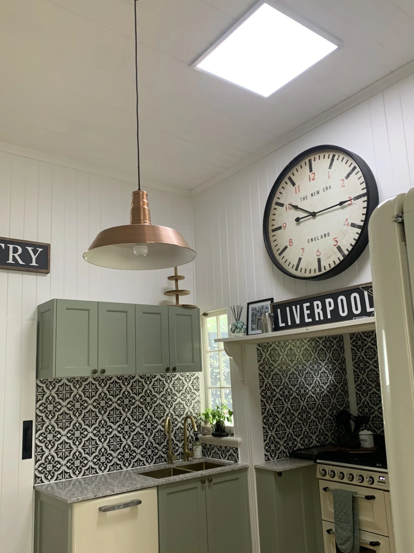 Kitchen with illume skylight, green cabinets, patterned backsplash, large wall clock, pendant light, and "Liverpool" sign