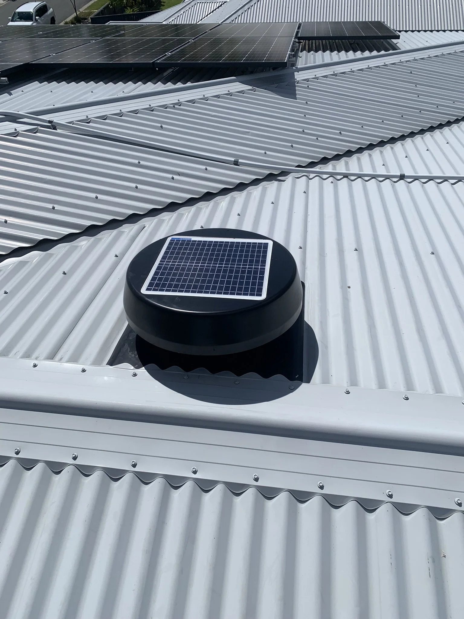 Corrugated metal roof with solar panels and a small solar-powered domed vent. 