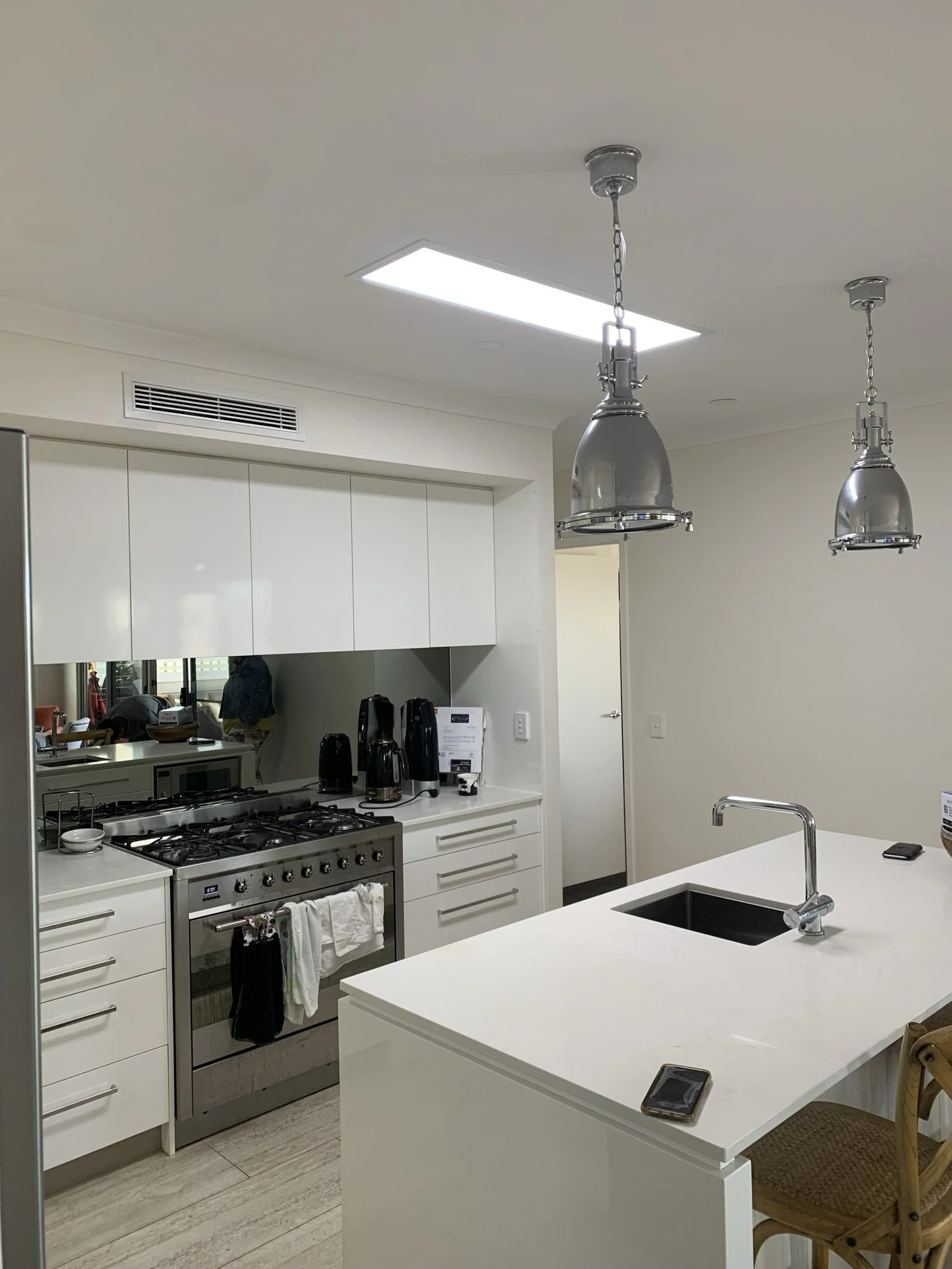 Modern kitchen with an illume skylight, white cabinets, stainless steel appliances, pendant lights, and a central island with a sink and seating.
