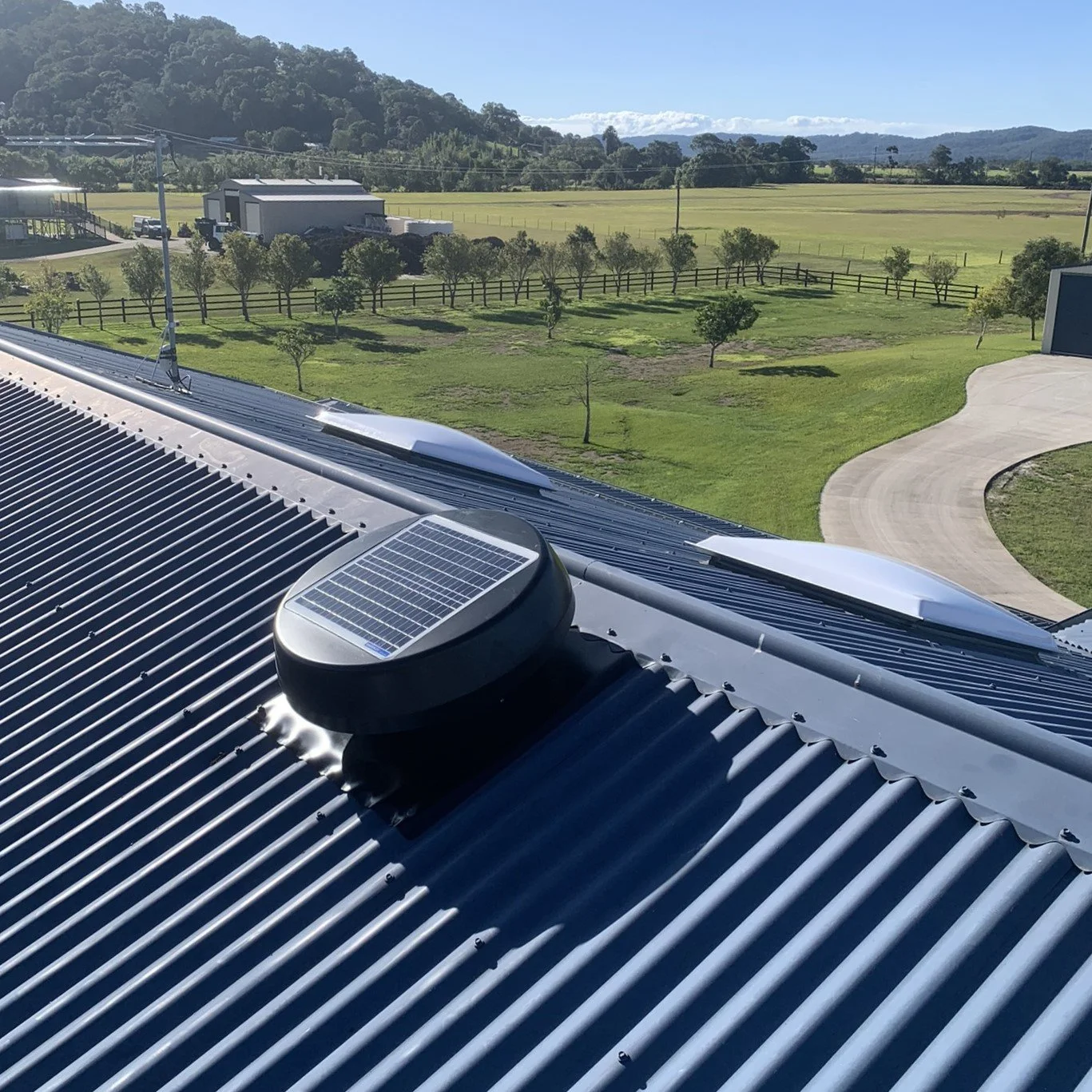 Solar-powered roof vent on a corrugated metal roof with rural landscape in the background.