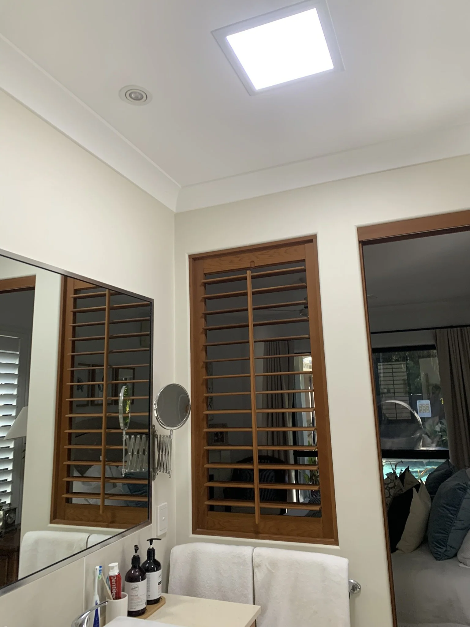 Bathroom with wooden shutters, a large mirror, toiletries on a counter, a towel on a rack and a skylight from illume.