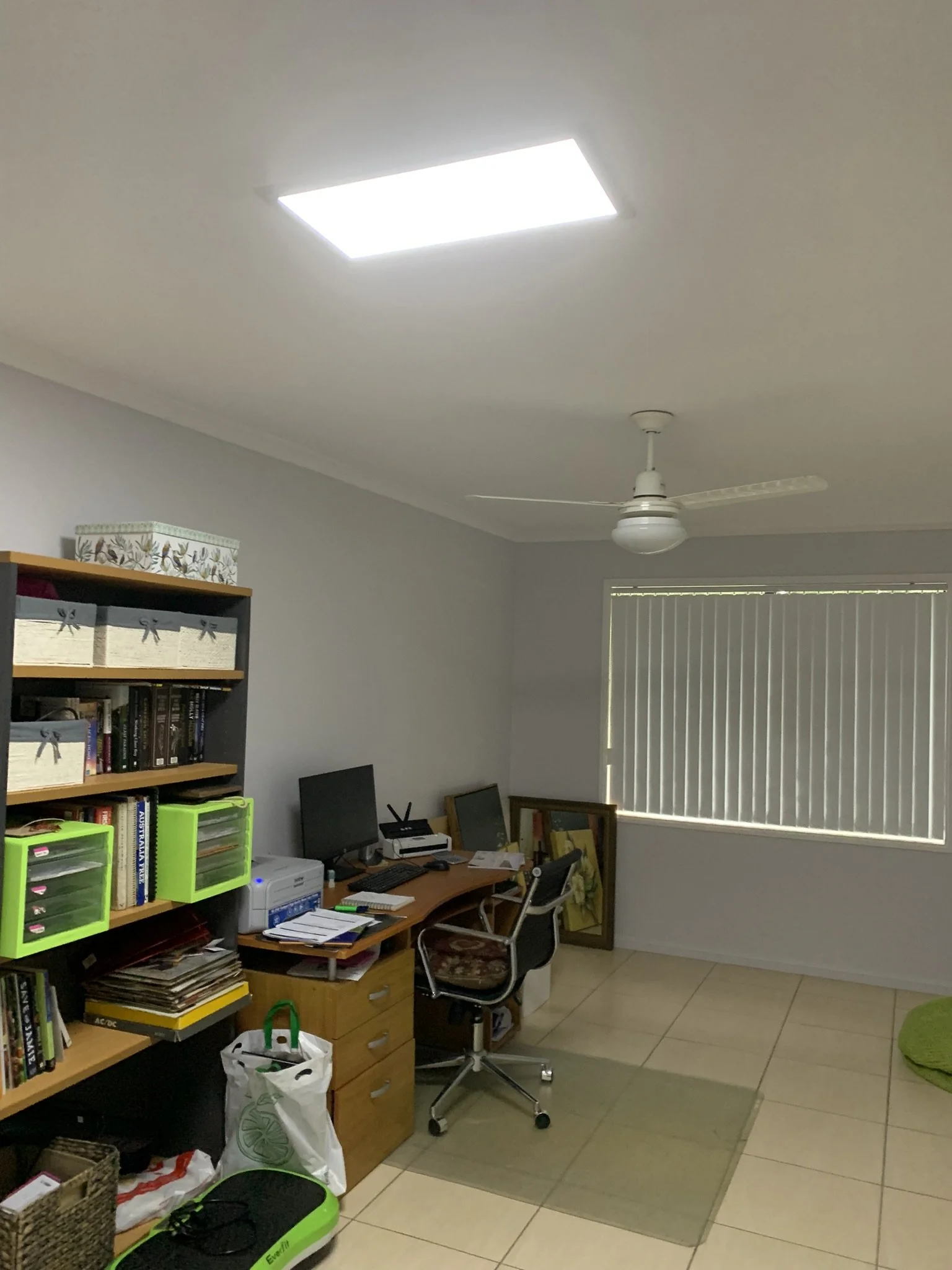 Home office with desk, computer, office chair, bookshelves, and ceiling fan. A square skylight illuminates the space.