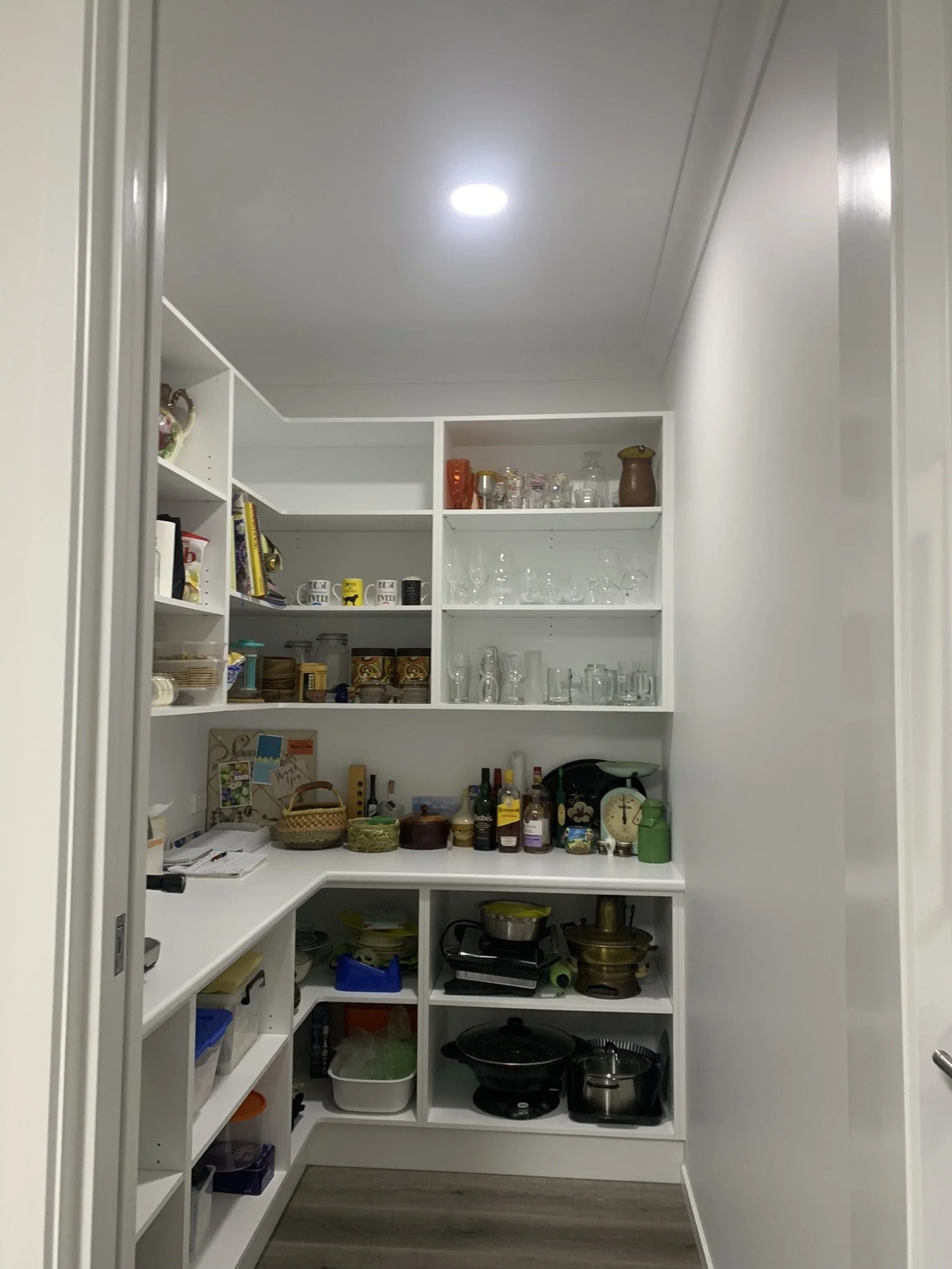 Organized pantry with an illume skylight, shelves, glassware, kitchenware, and food items.
