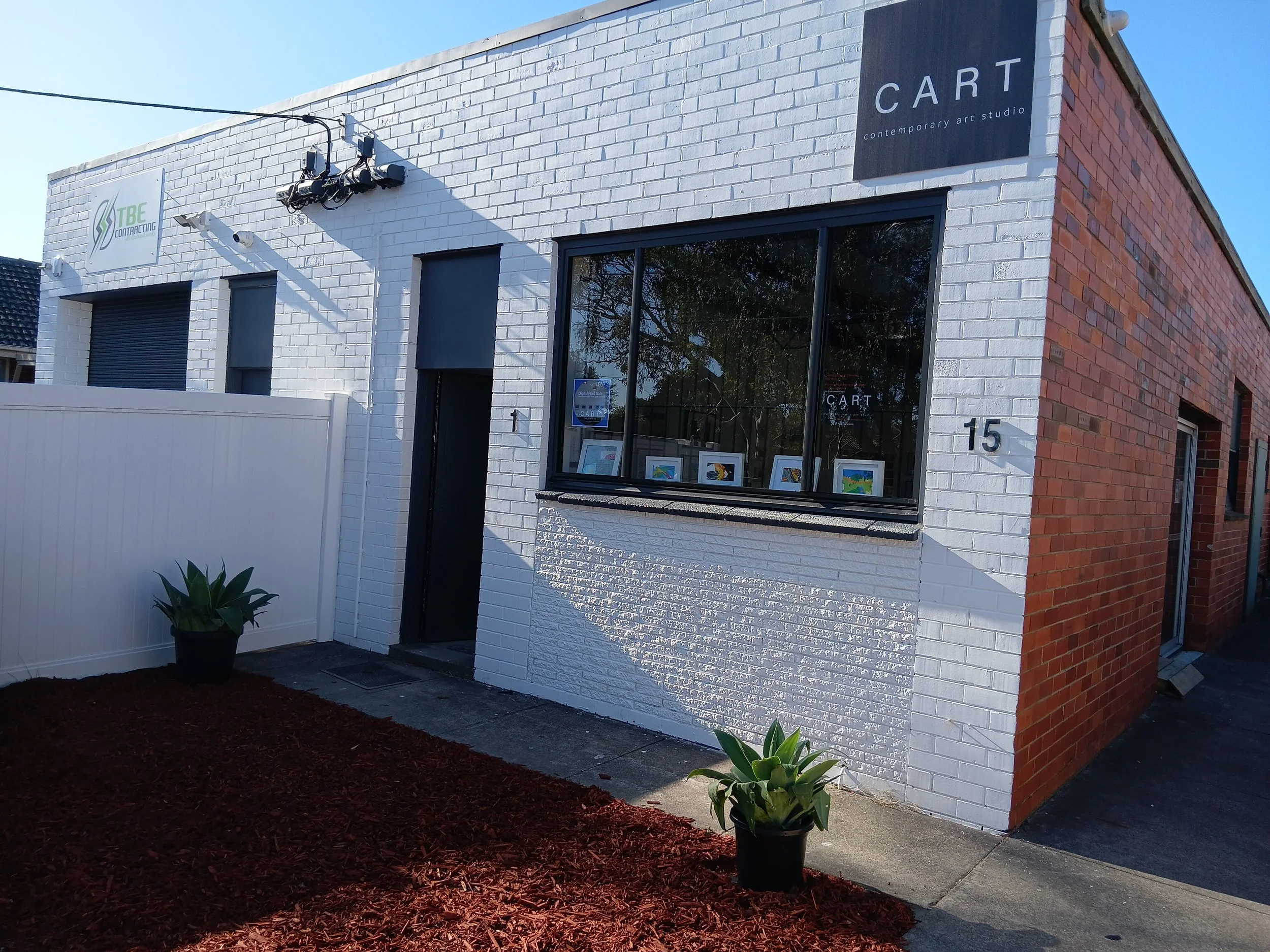 A commercial building with a brick exterior and a white painted section, housing an art studio called 'CART', located at 15, with a sidewalk in front and a small fence on the right side.