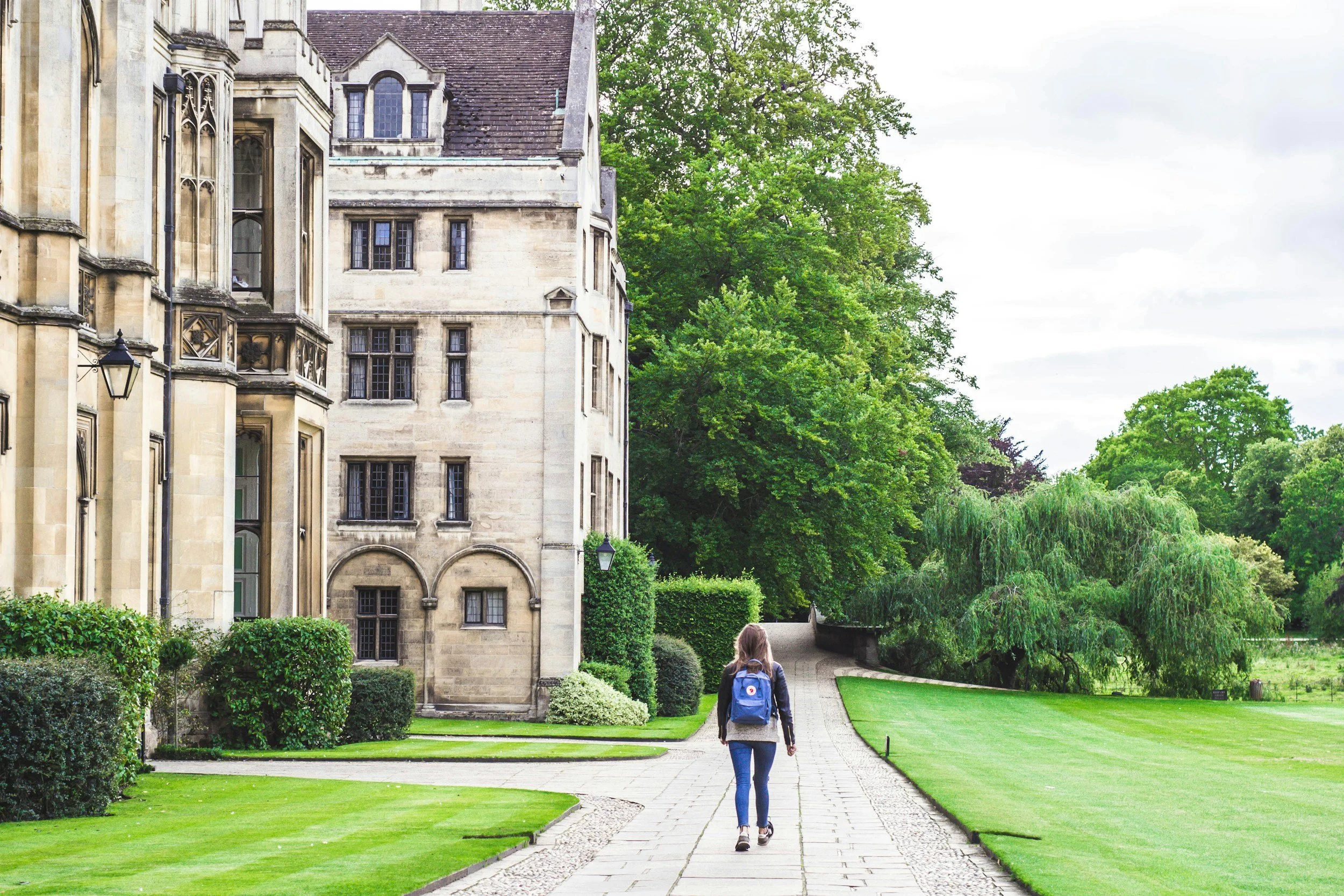 College girl walking toward campus building. English teacher offering service to coach students writing college admission essays.
