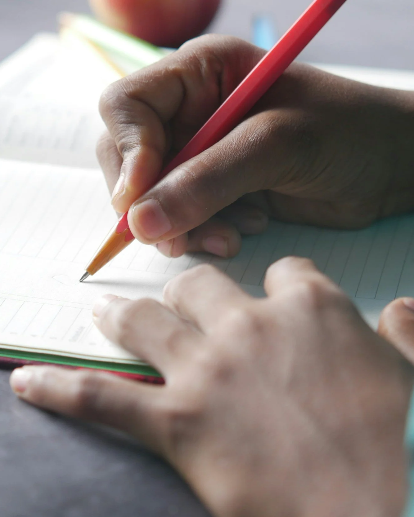 A person writing in a notebook with a red pencil.