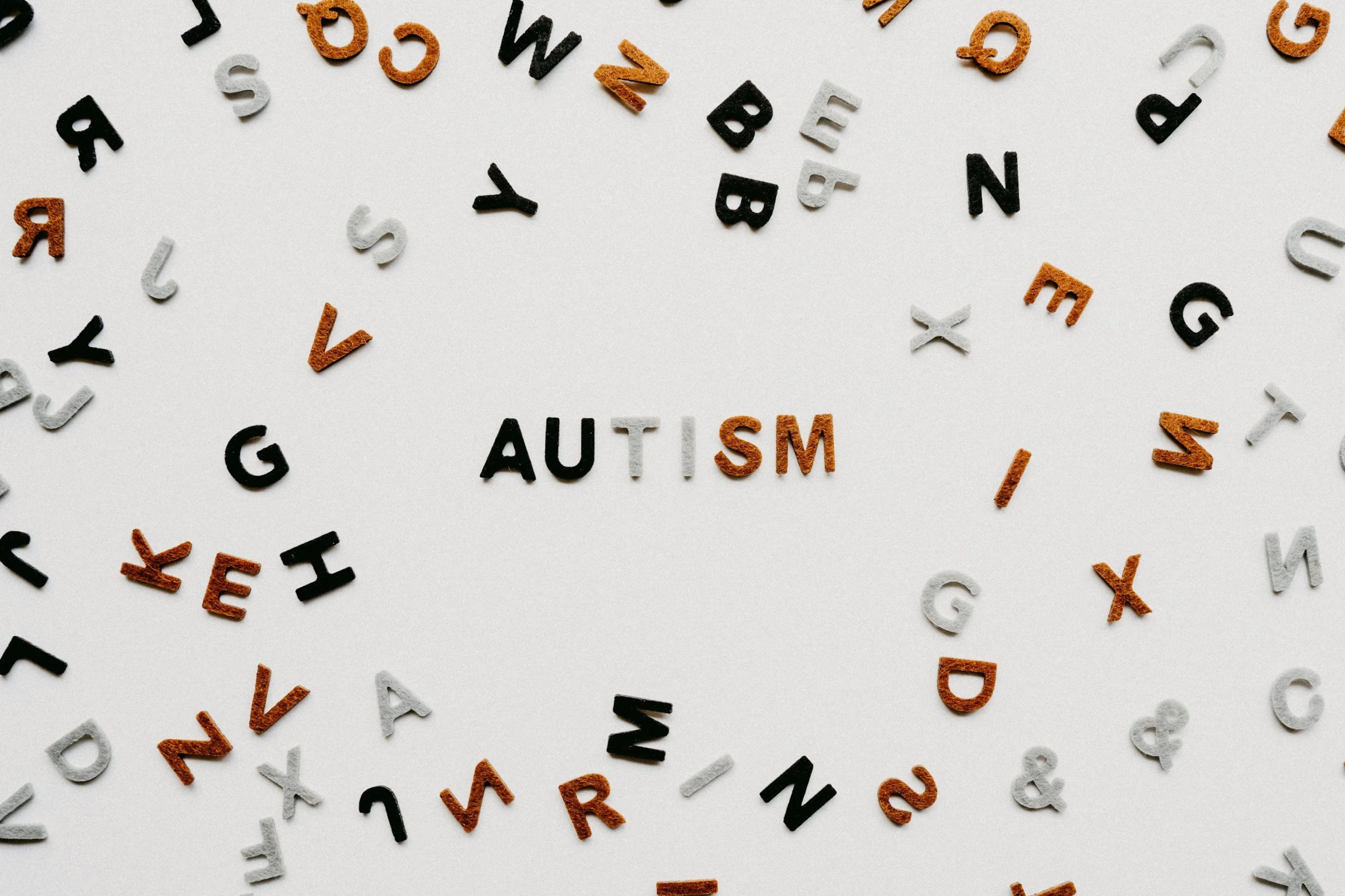 Colorful letter tiles spelling out 'Autism' surrounded by scattered black, white, and orange letter tiles on a white background.