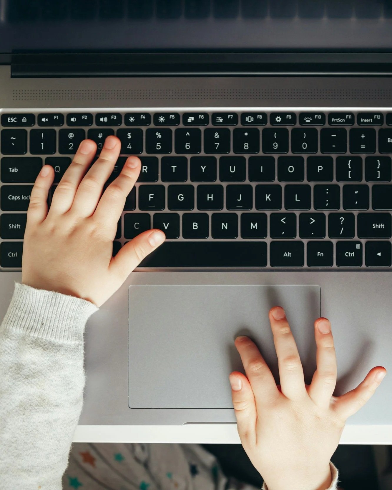 A child's hands are navigating a laptop keyboard to take an academic achievement test.