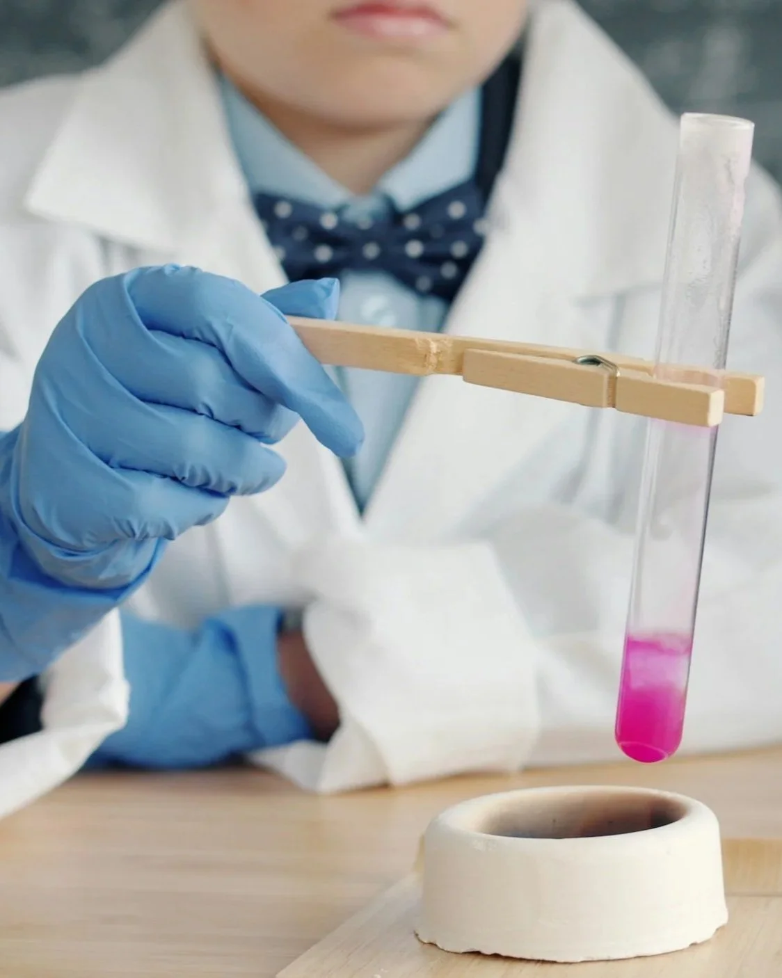A little boy in a lab coat is performing a chemical science experiment with gloves and a test tube.