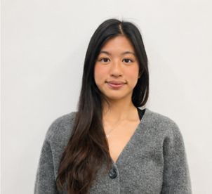 Smiling person wearing a cream knitted sweater against a plain wall background.
