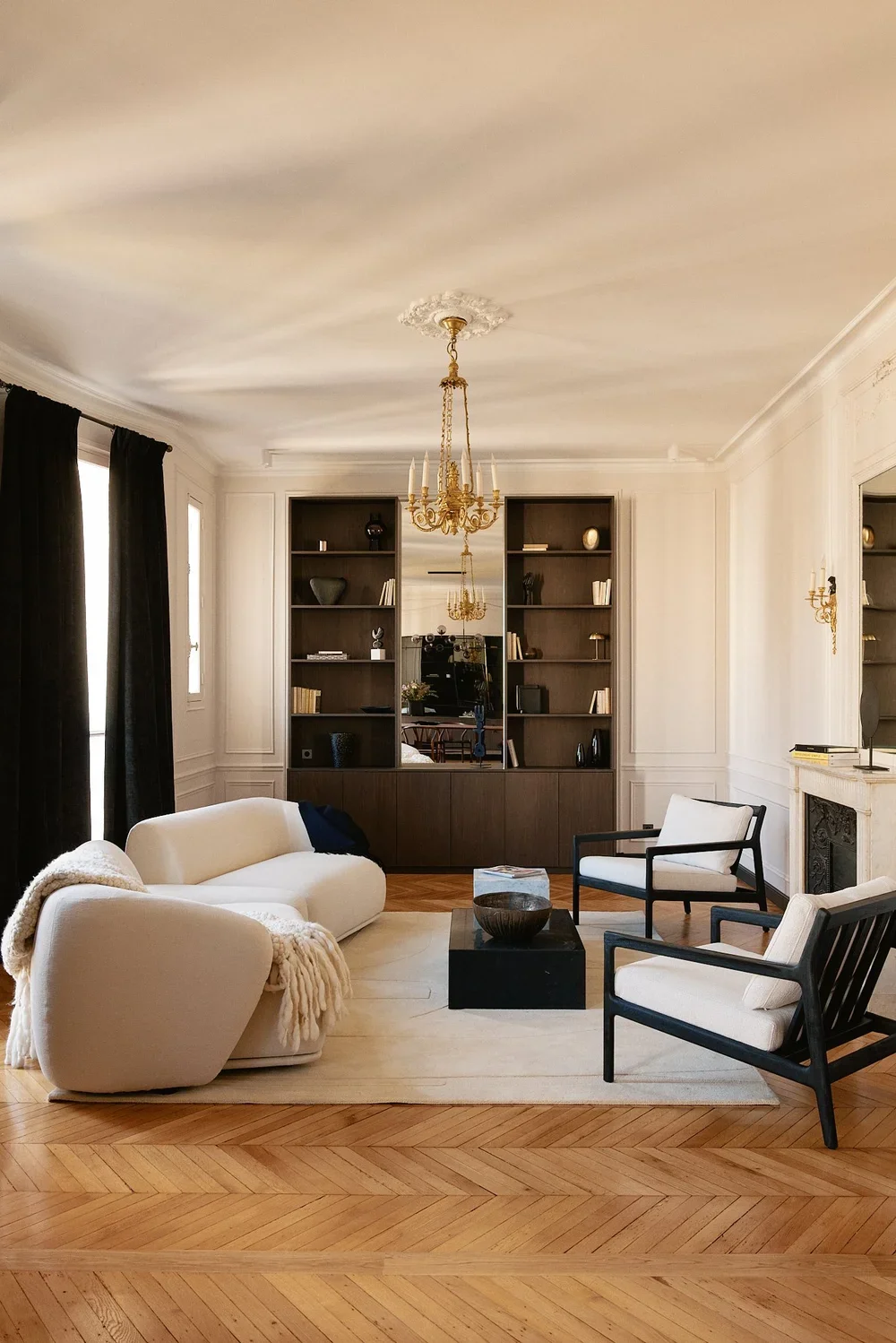 Living room with a white sofa, black armchairs, a black coffee table, dark built-in bookshelves, a chandelier, and hardwood floors.