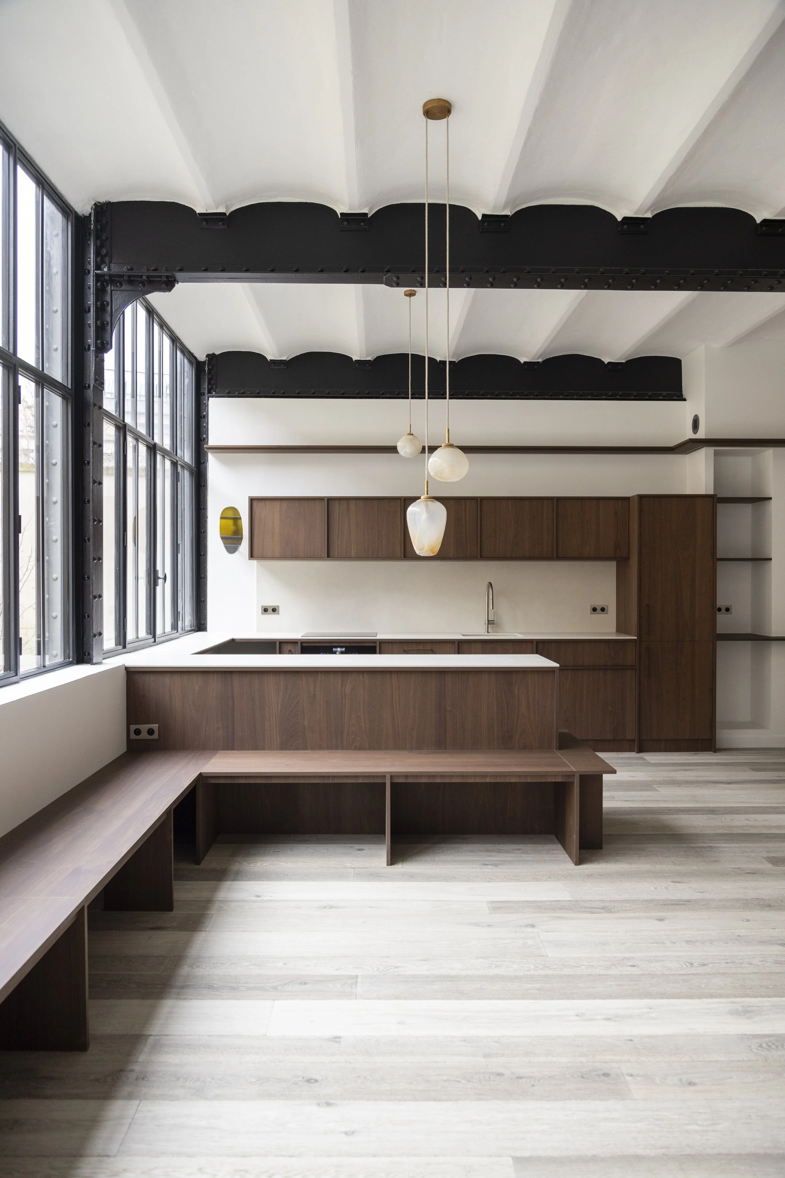 Modern kitchen with wood cabinets, black countertop, large windows, and hanging pendant lights with marble-like shades.
