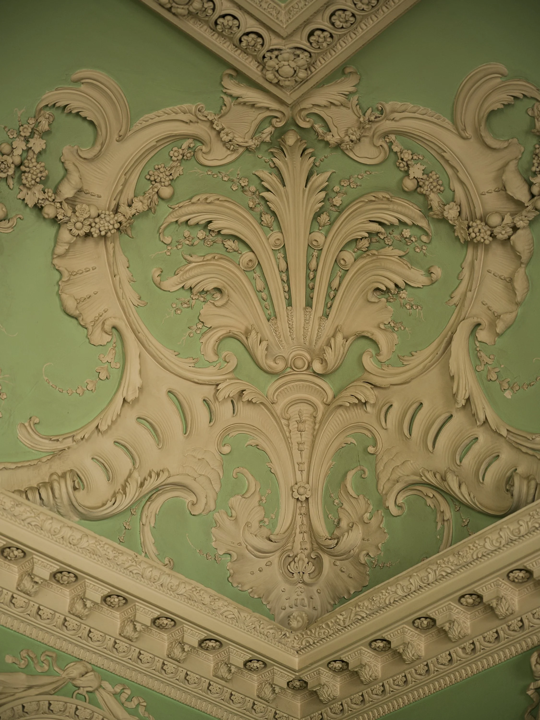 Ornate ceiling with intricate plasterwork and floral motifs on a green background.