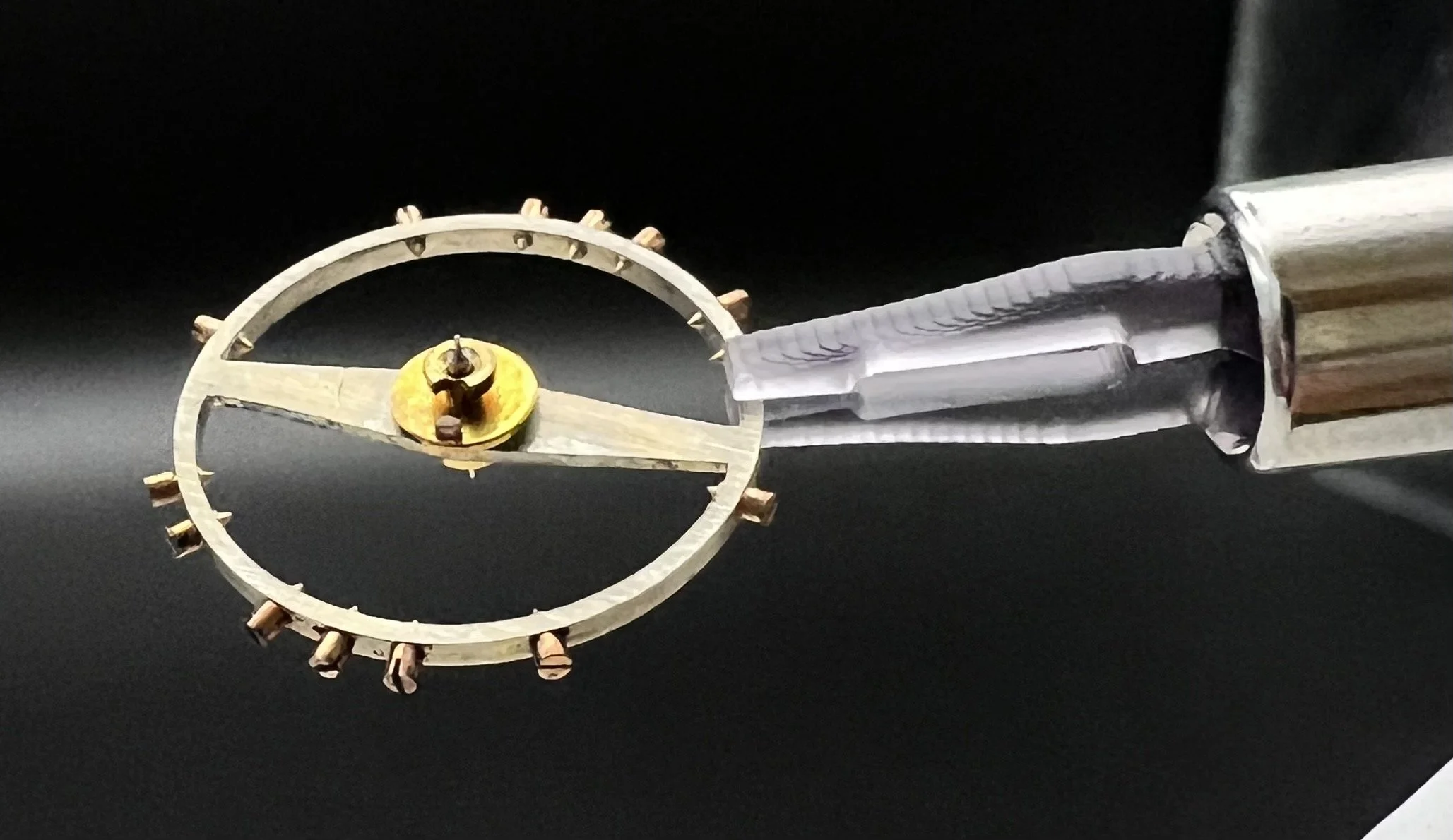 Roue dentée d'une montre mécanique tenue par une pince.