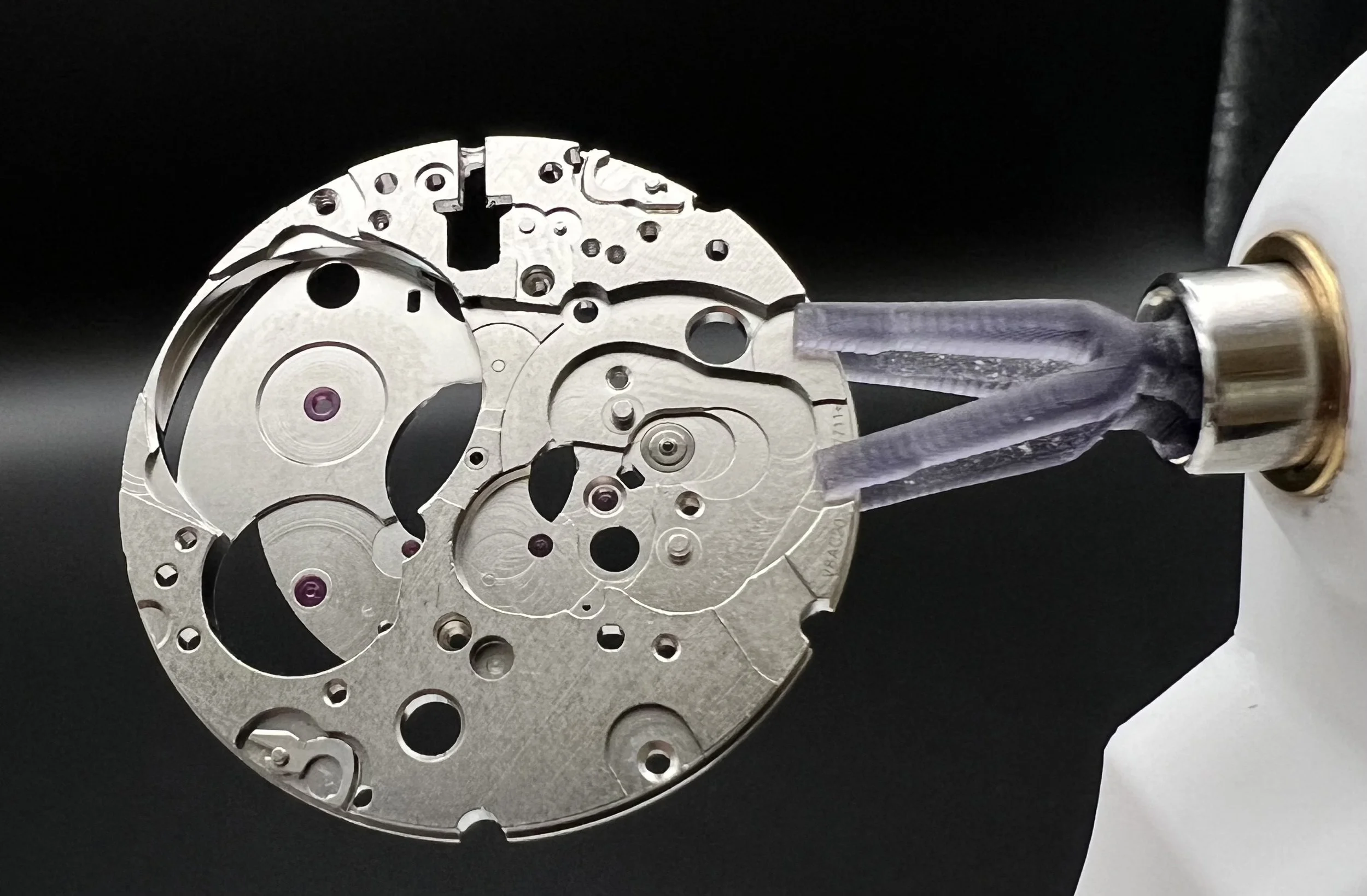Mouvement de montre mécanique en cours d'assemblage avec un outil de manipulation tenant la pièce en métal argenté.